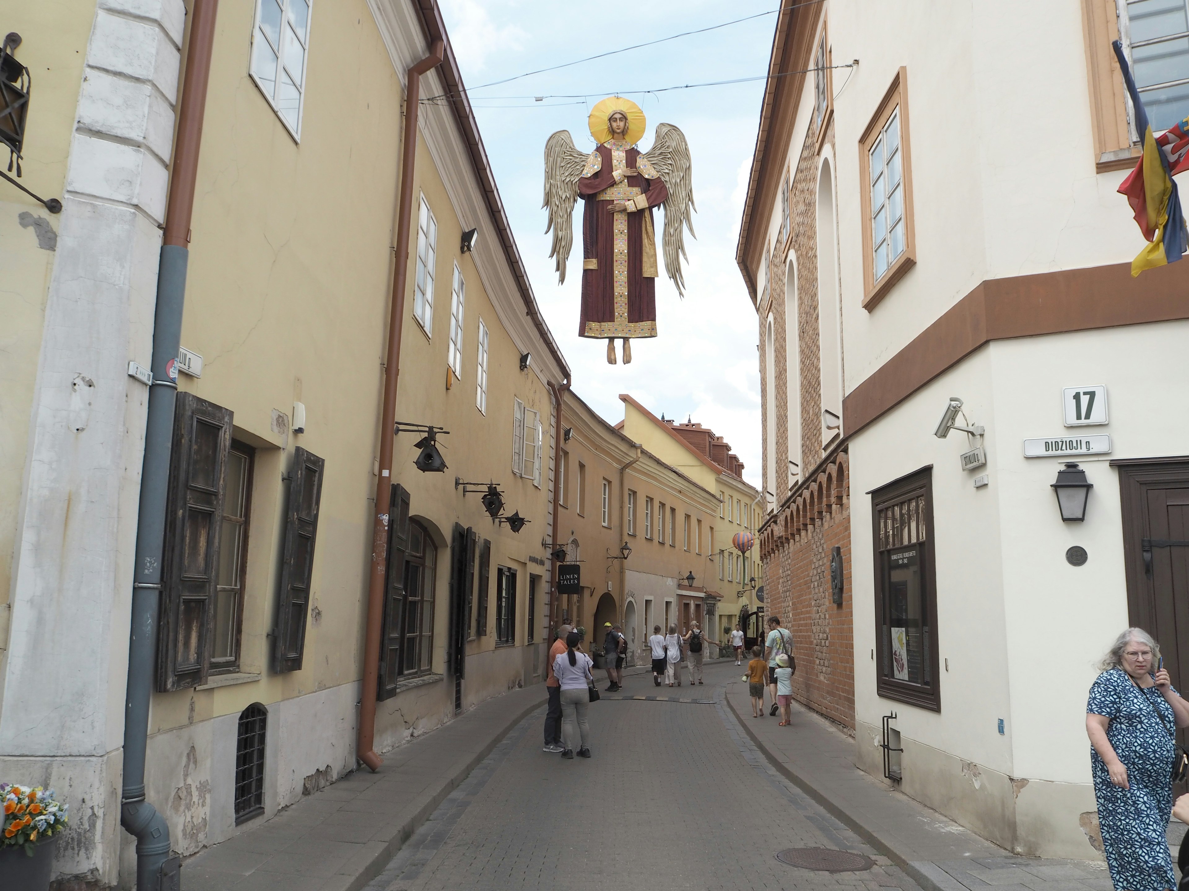 Street scene featuring hanging angel figure and pedestrians