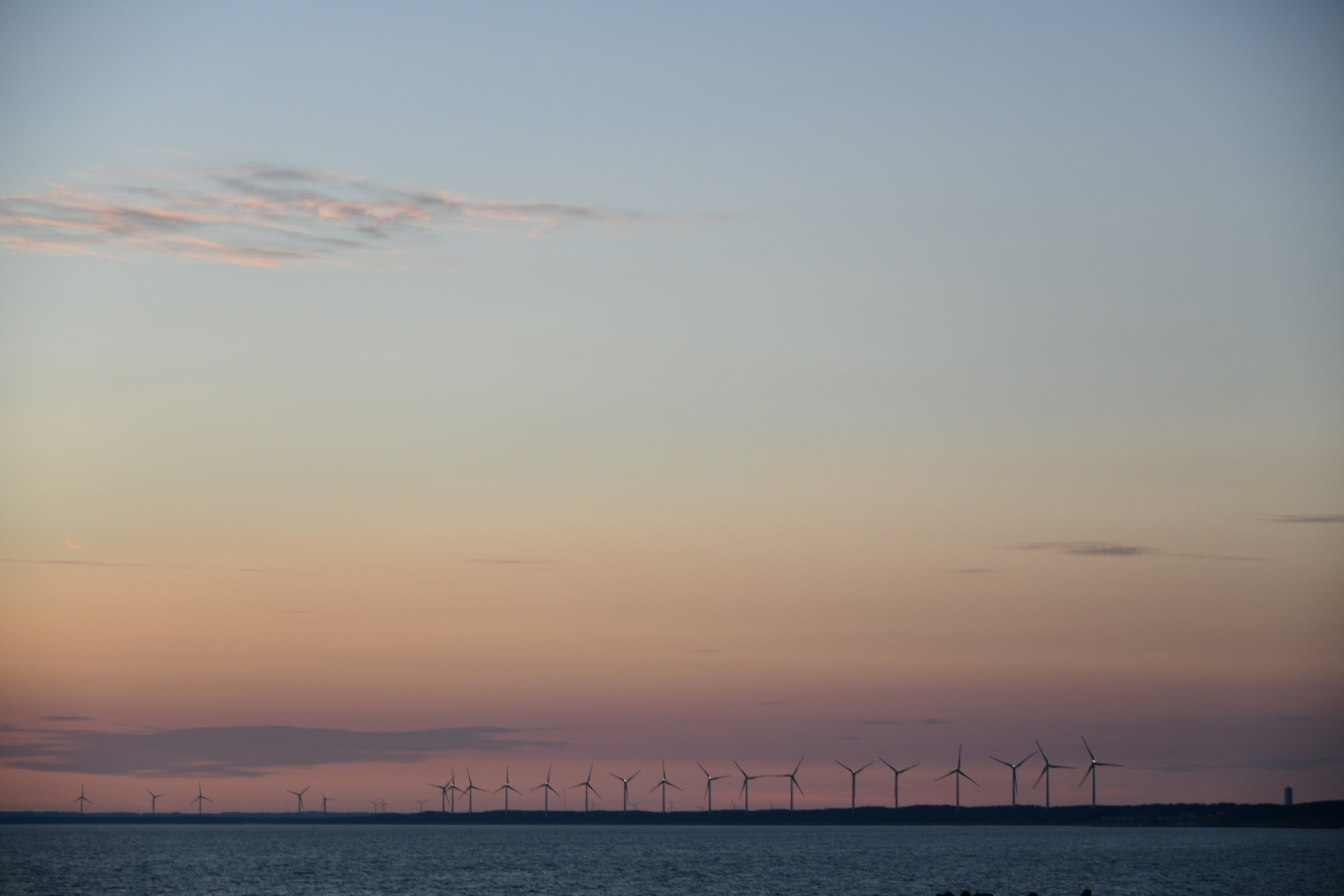 Sonnenuntergangshimmel über dem Ozean mit Windkraftanlagen im Hintergrund