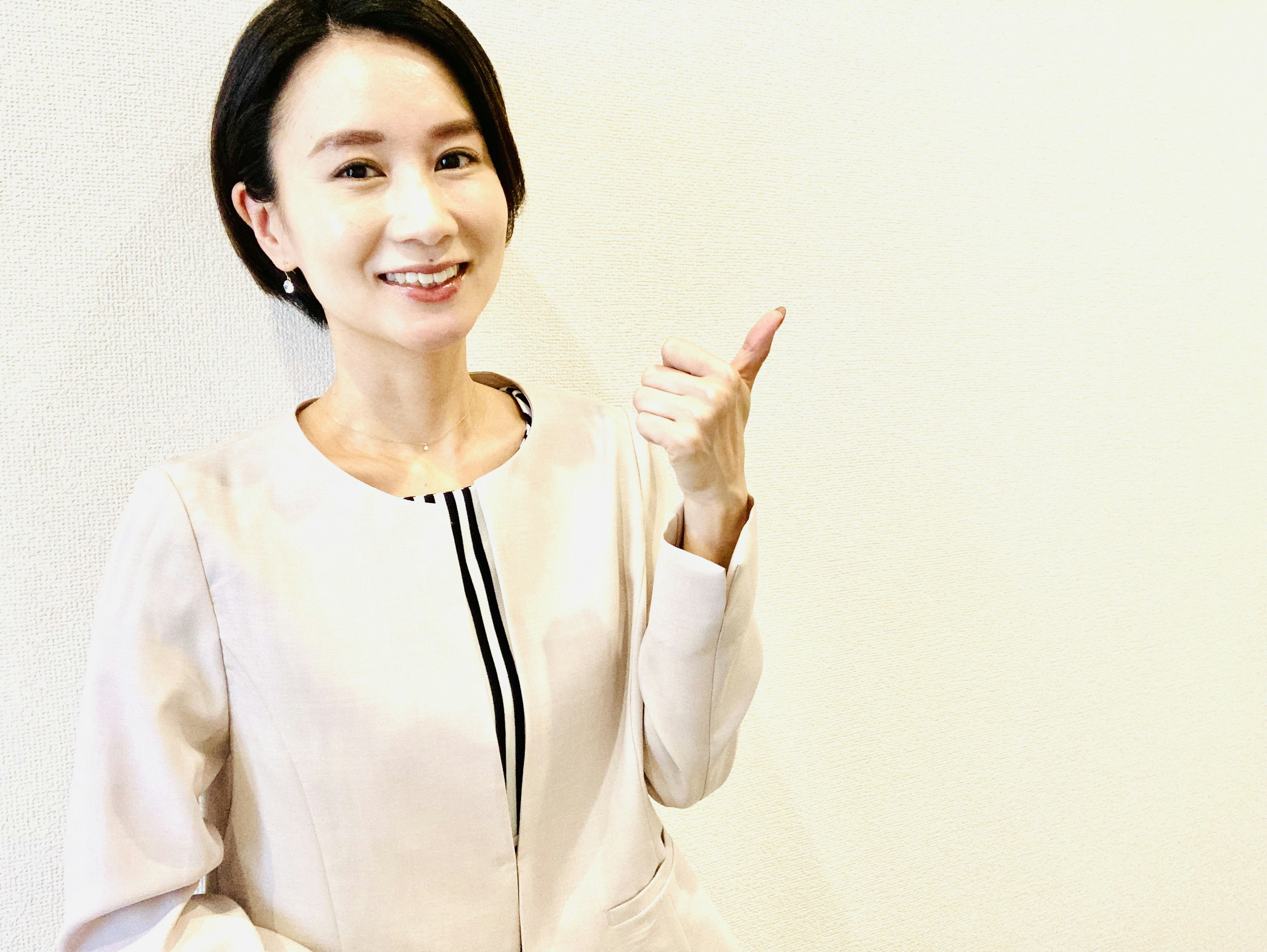 A woman smiling and giving a thumbs up in front of a white background