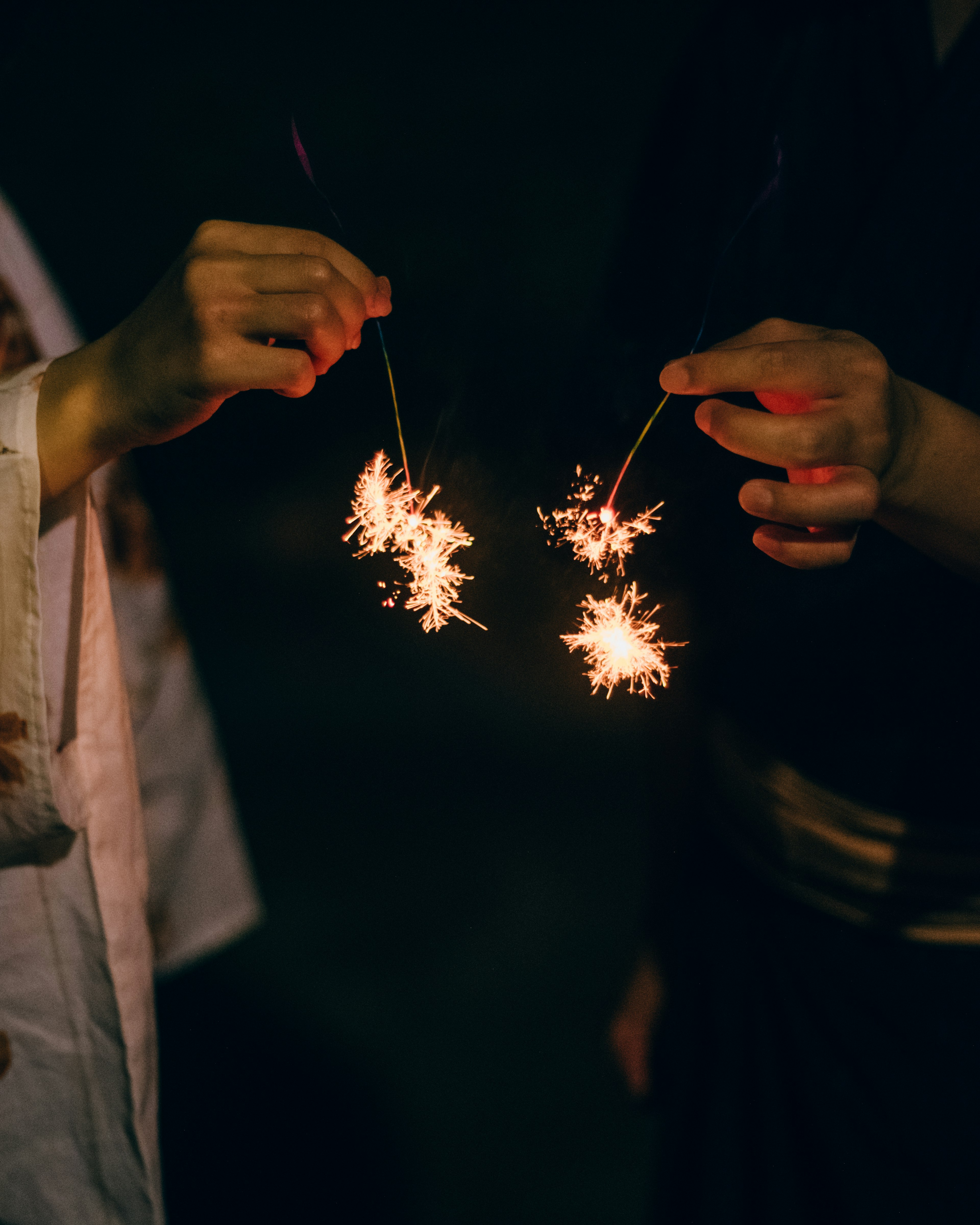 Two hands holding sparklers in the dark