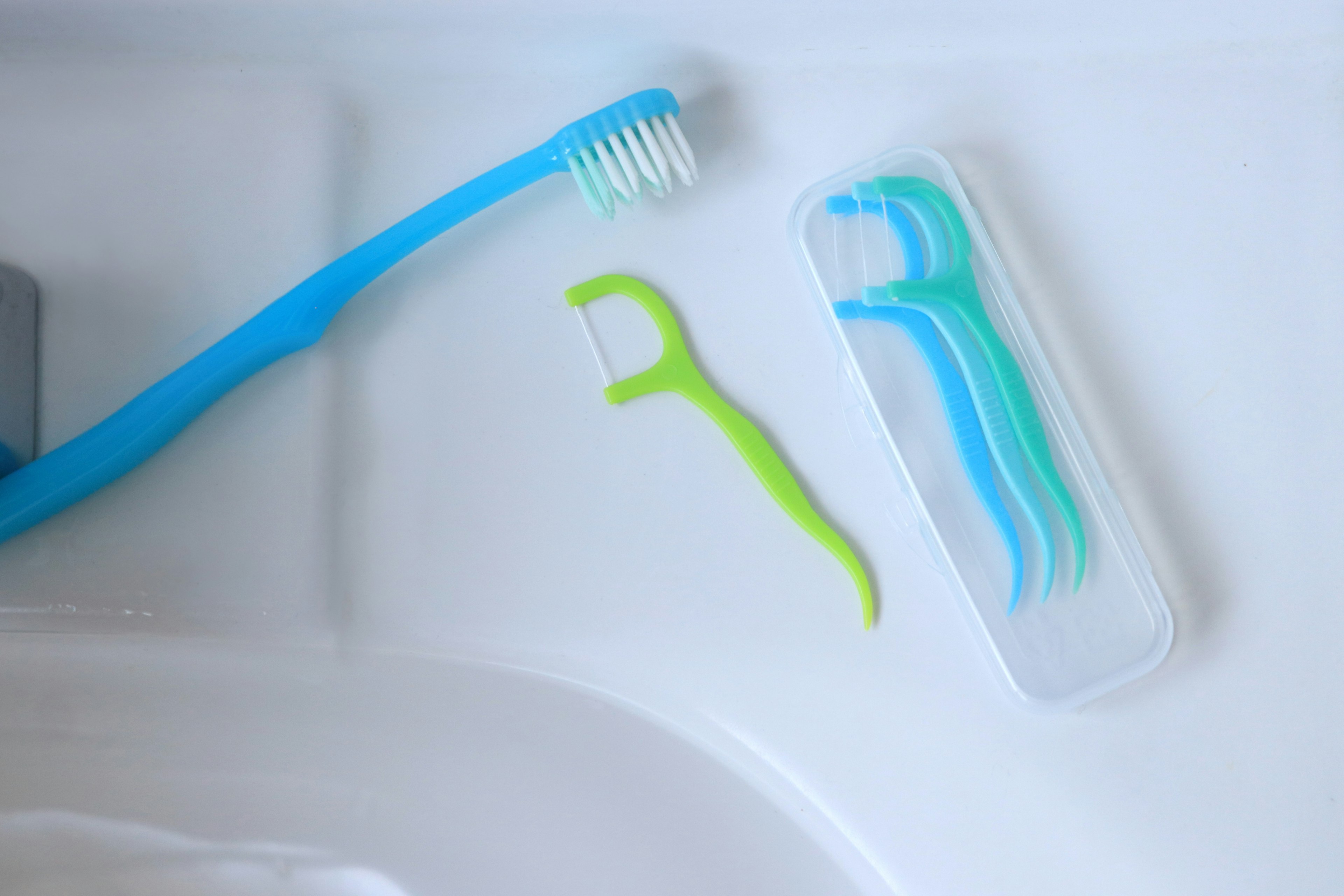 Blue toothbrush and green floss pick on a sink