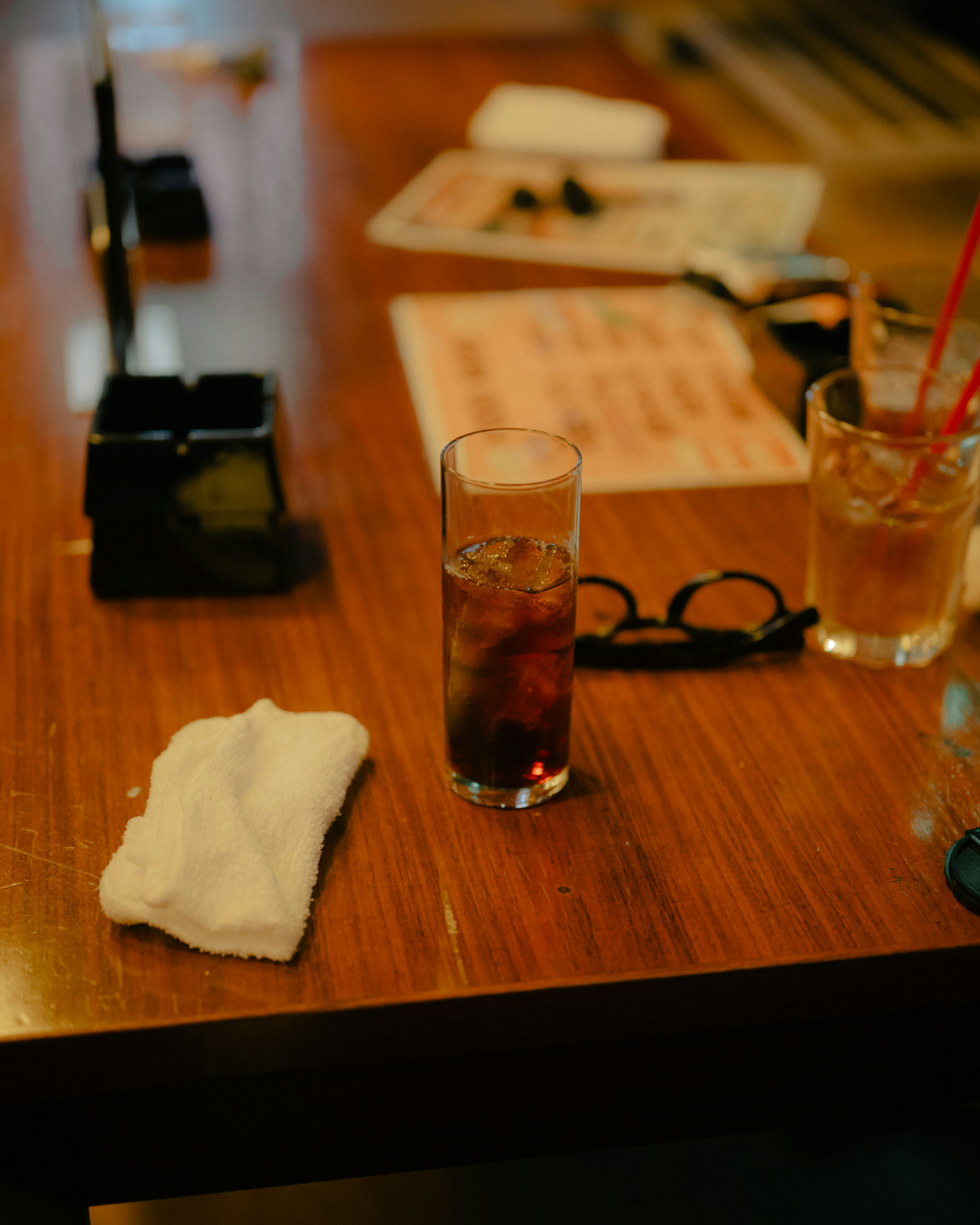 Un vaso de bebida sobre una mesa de madera con una servilleta y gafas cerca