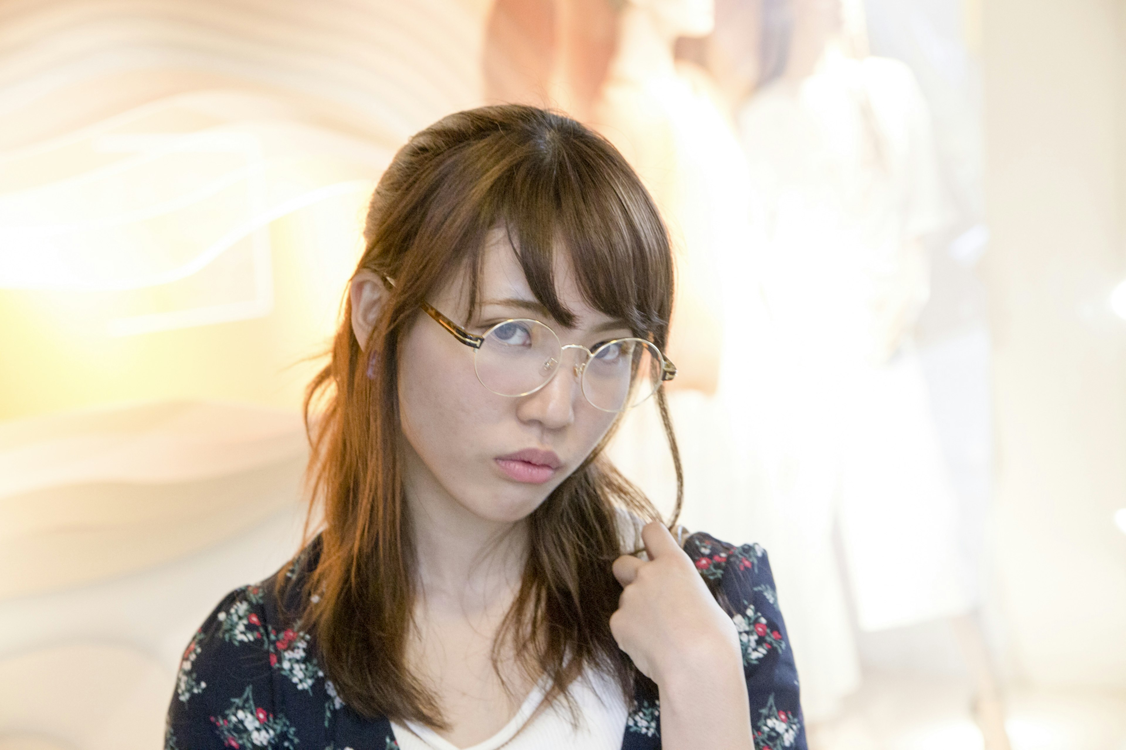 A woman wearing glasses with a thoughtful expression pointing at herself