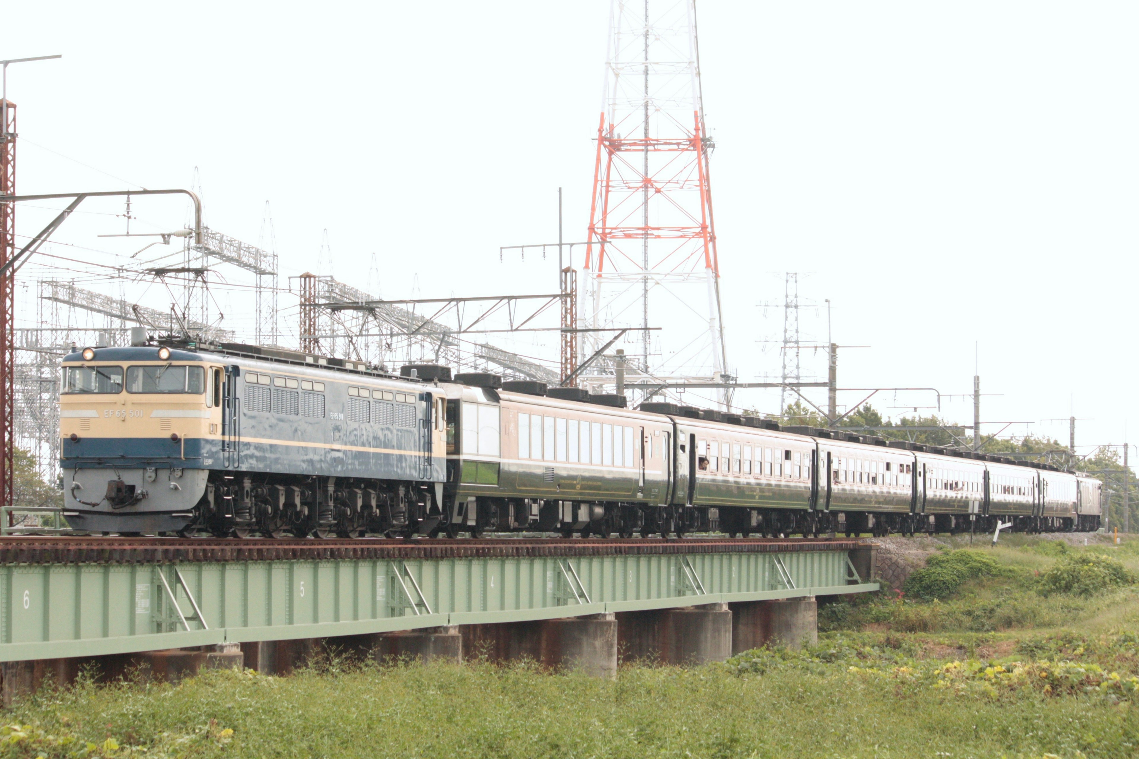 Blue electric locomotive pulling a long train over a bridge