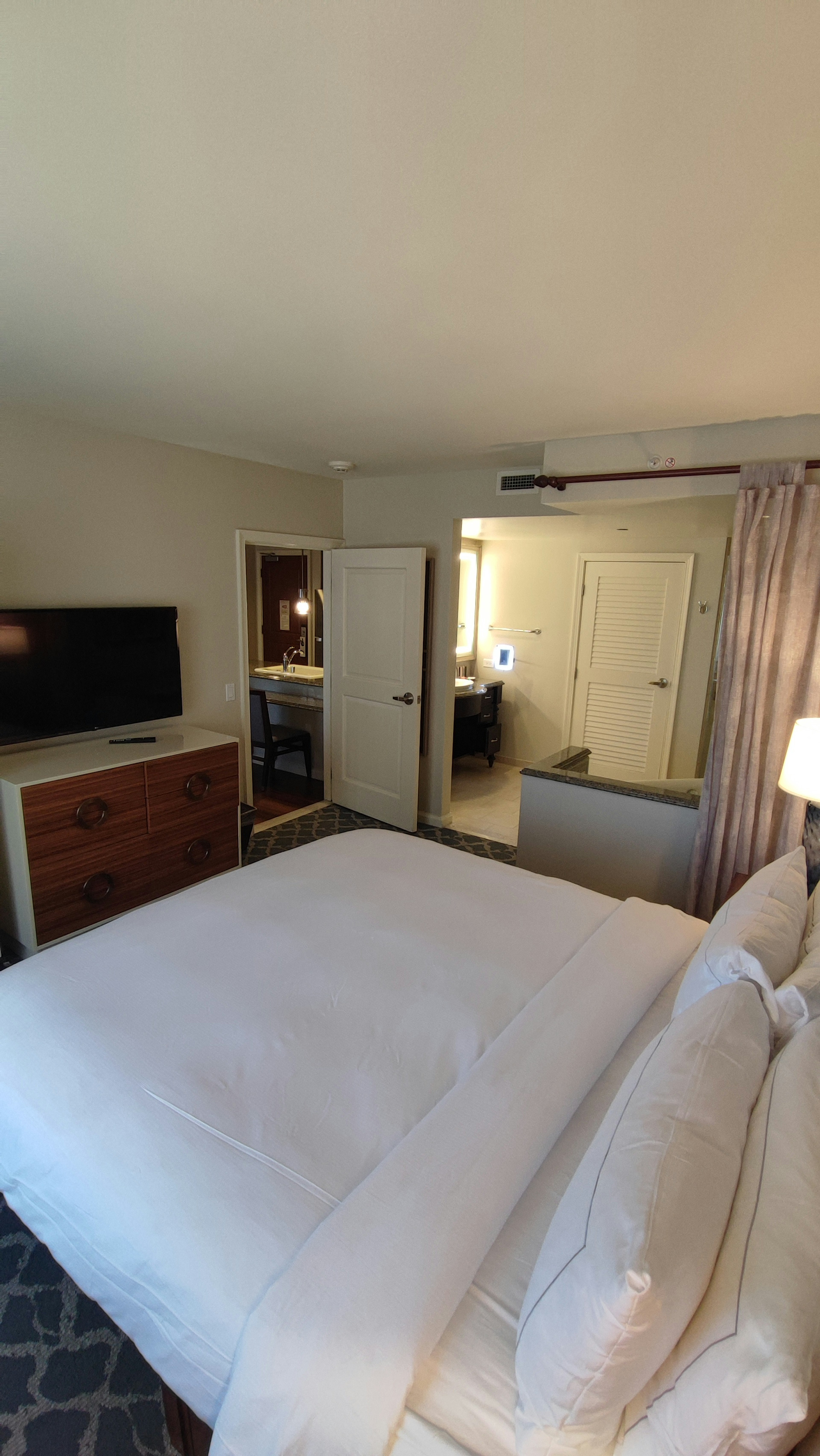 Bright bedroom interior featuring a white bed, television, furniture, and doors