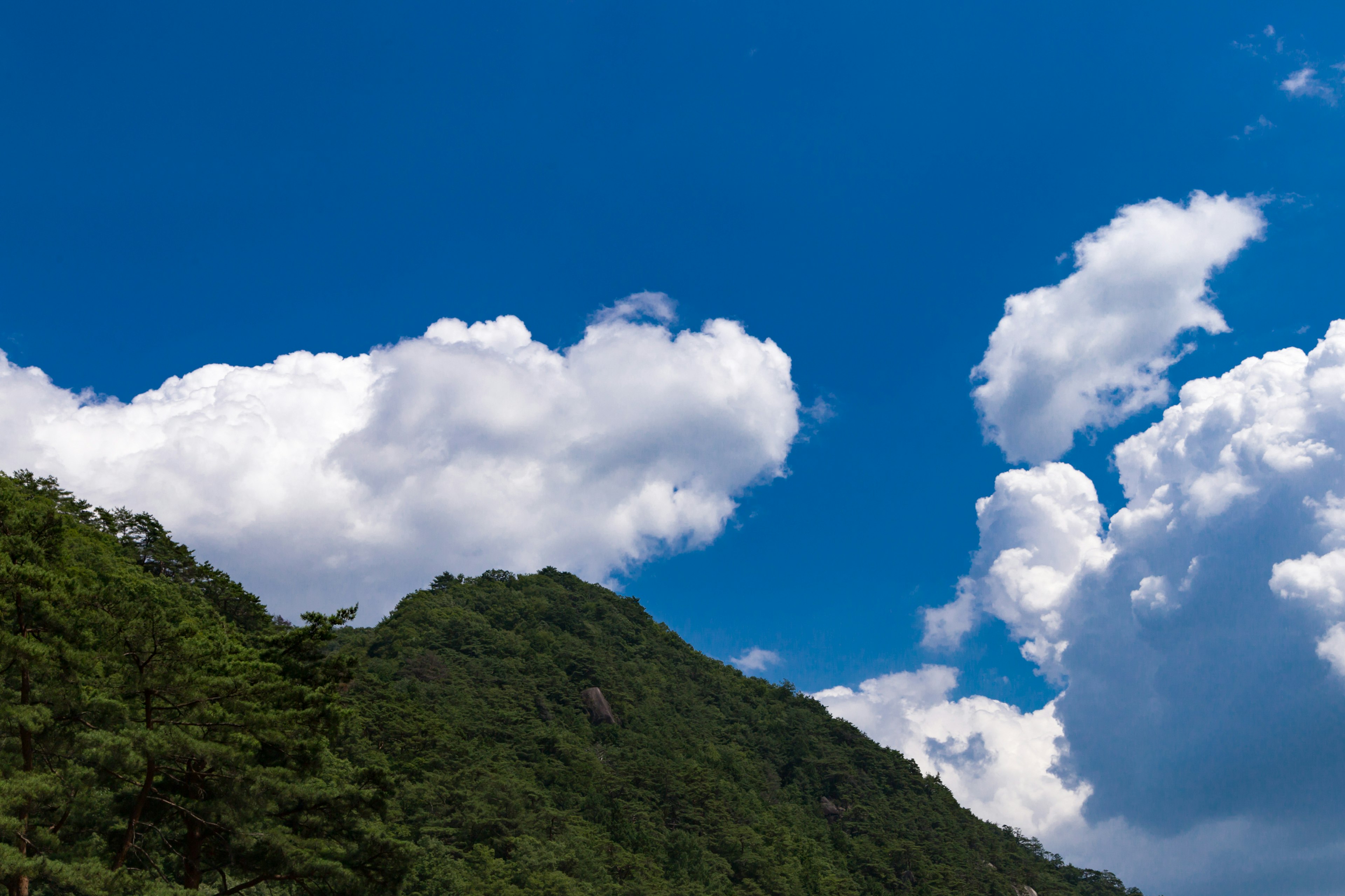 Landschaft mit einem grünen Berg unter einem hellblauen Himmel mit fluffigen weißen Wolken