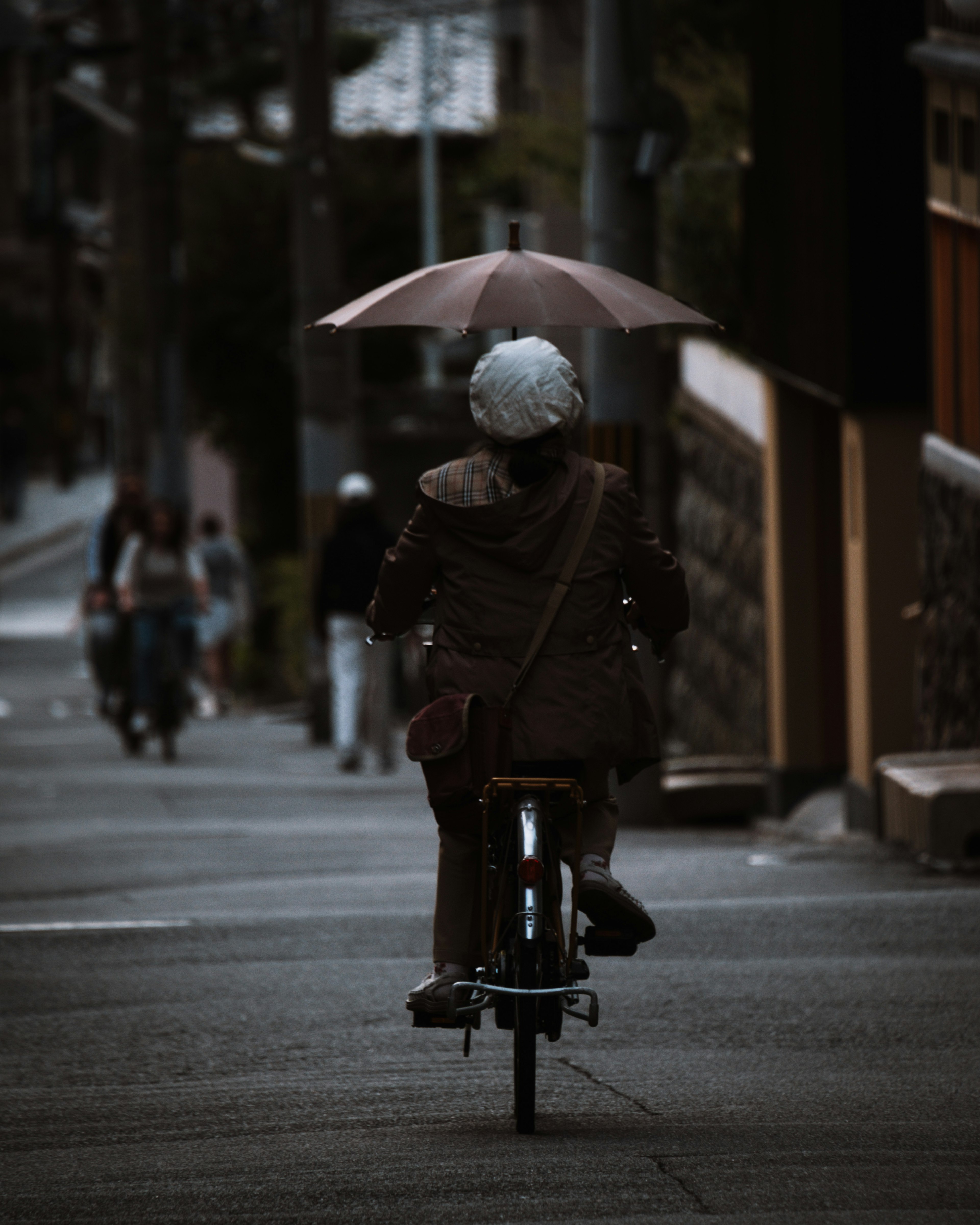 Person riding a bicycle with an umbrella in a street scene