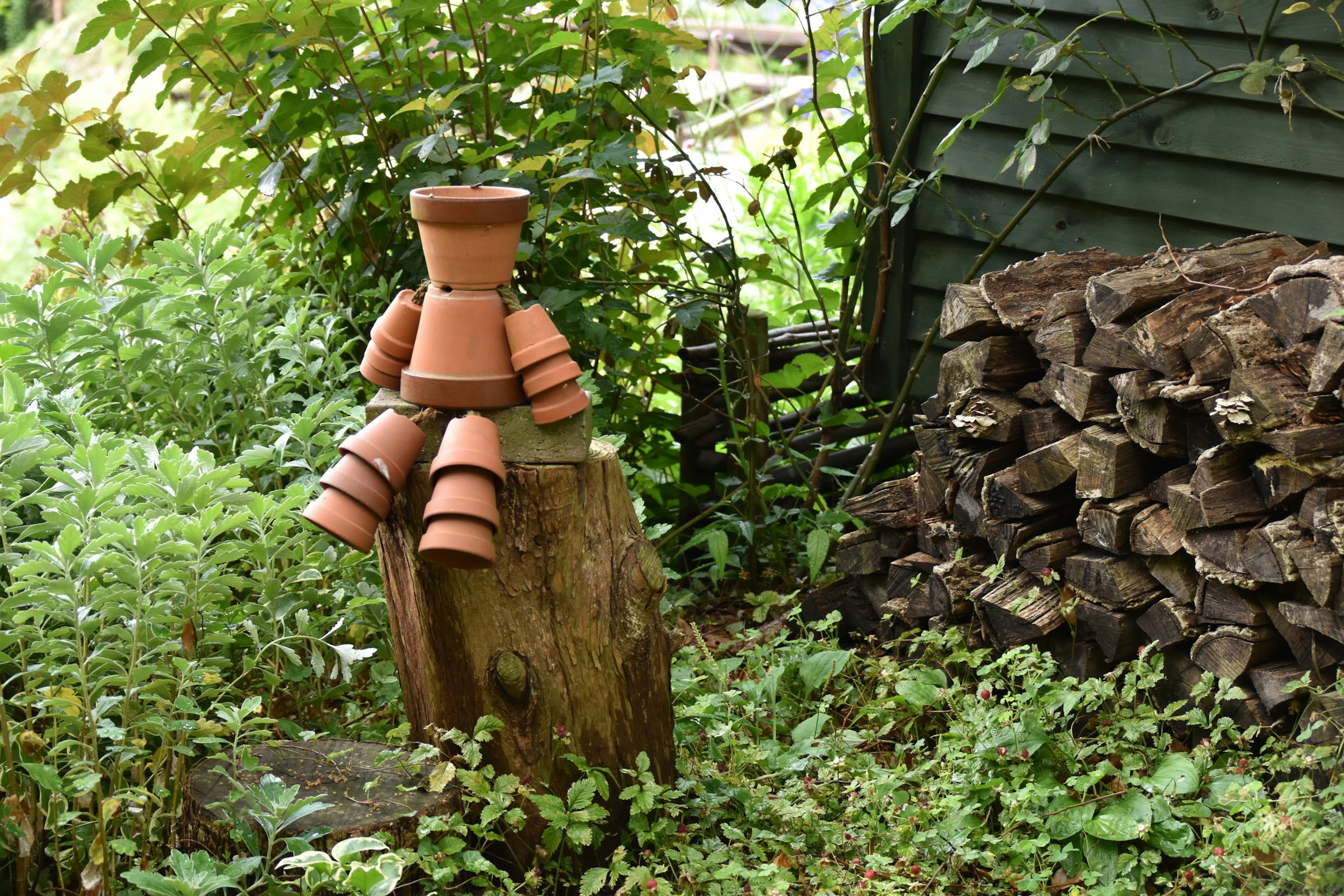 Una figura realizzata con vasi da fiori seduta su un ceppo in un giardino