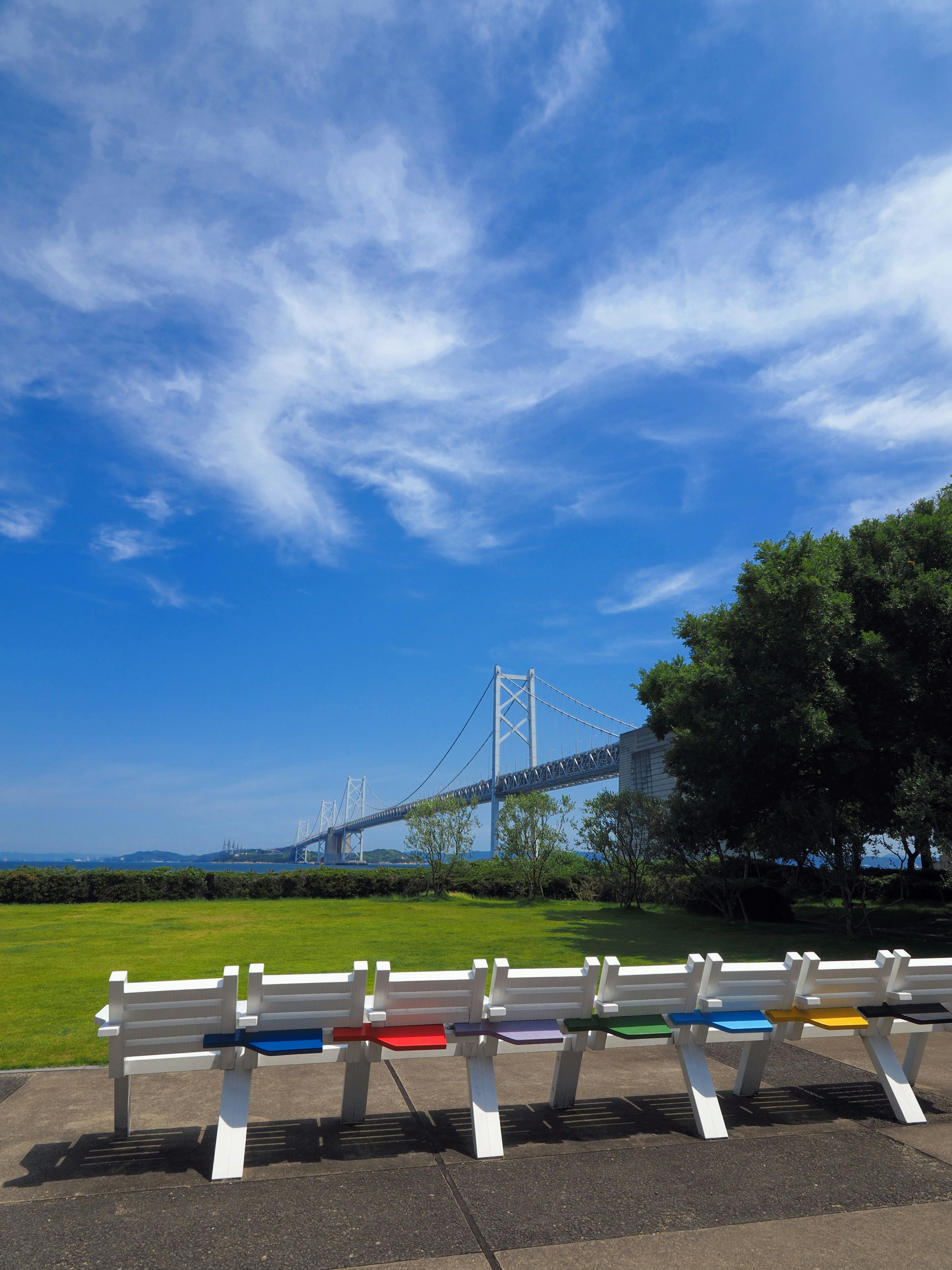 Colorful benches under a blue sky with white clouds and a bridge in the background