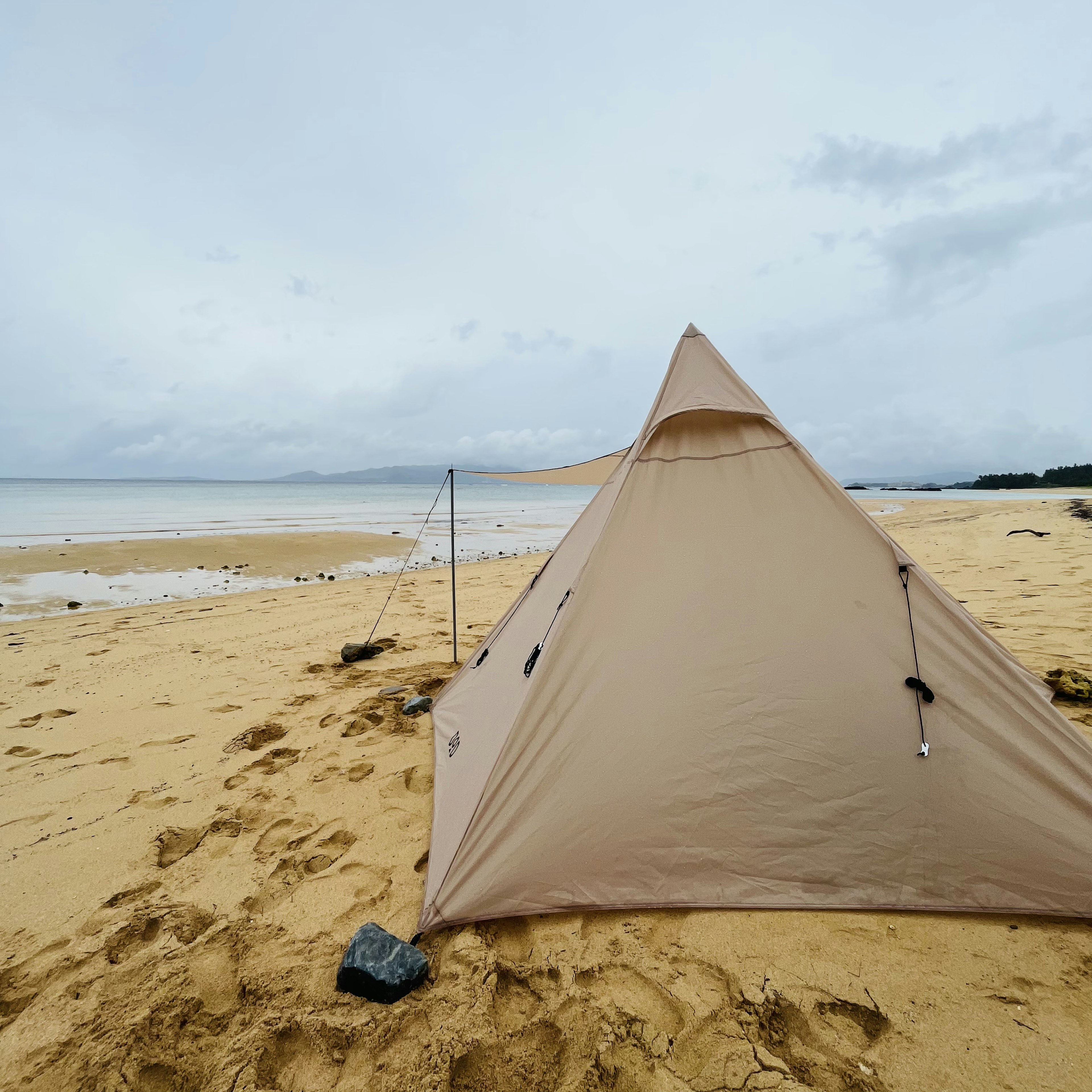 Tienda beige instalada en una playa con una orilla de arena