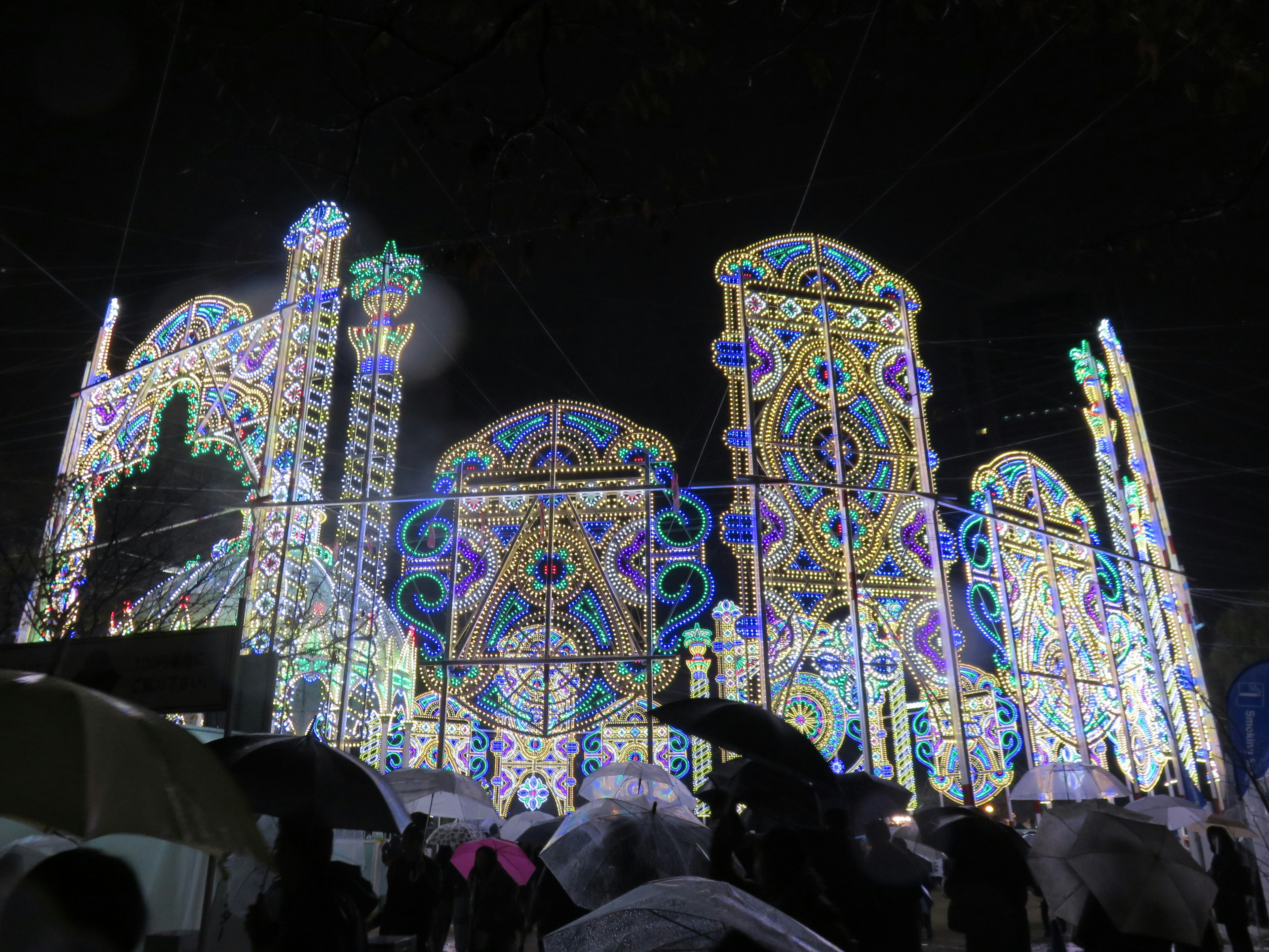 Edificios iluminados por la noche con personas con paraguas