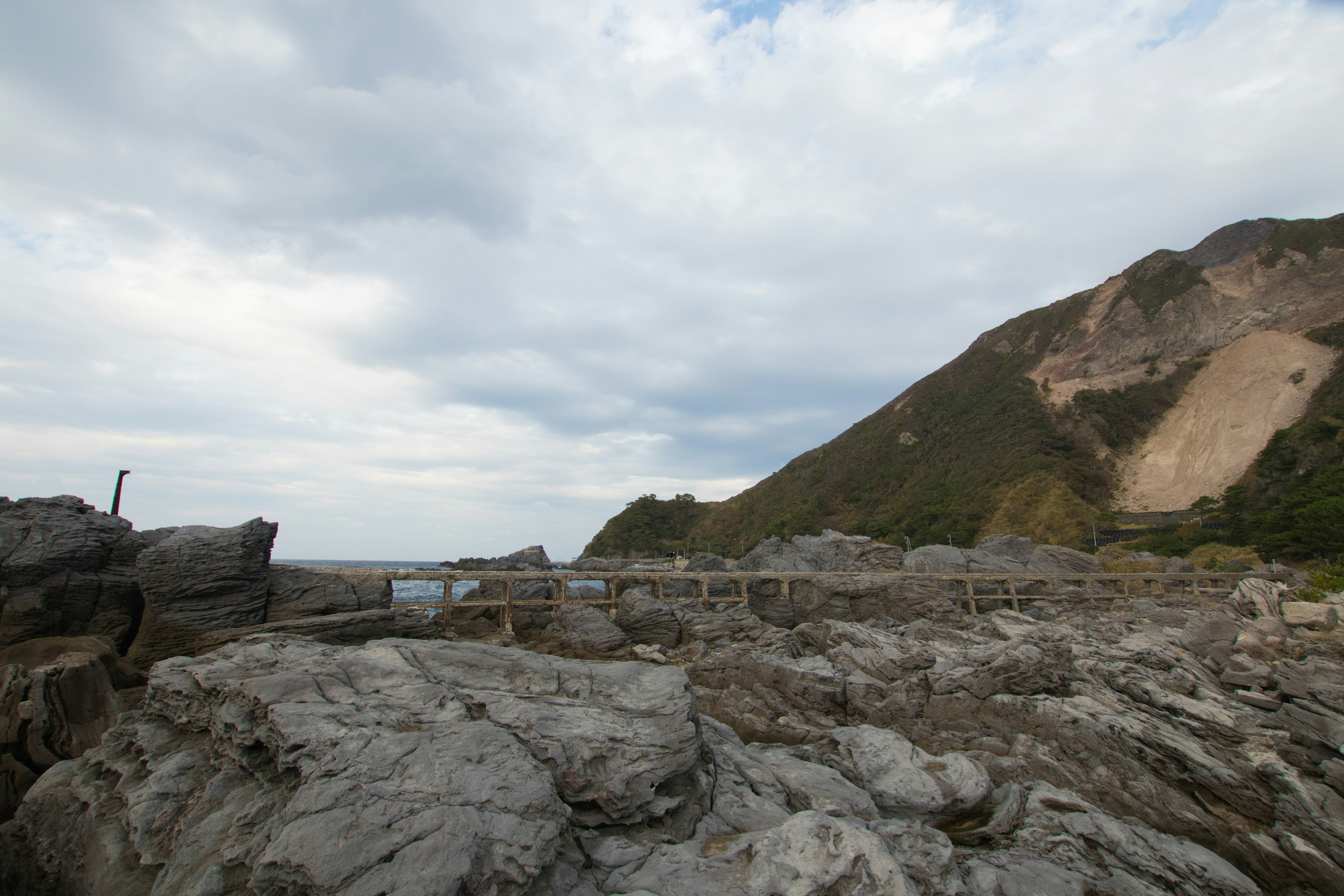 Costa rocosa con vista al océano cielo nublado y montaña verde al fondo