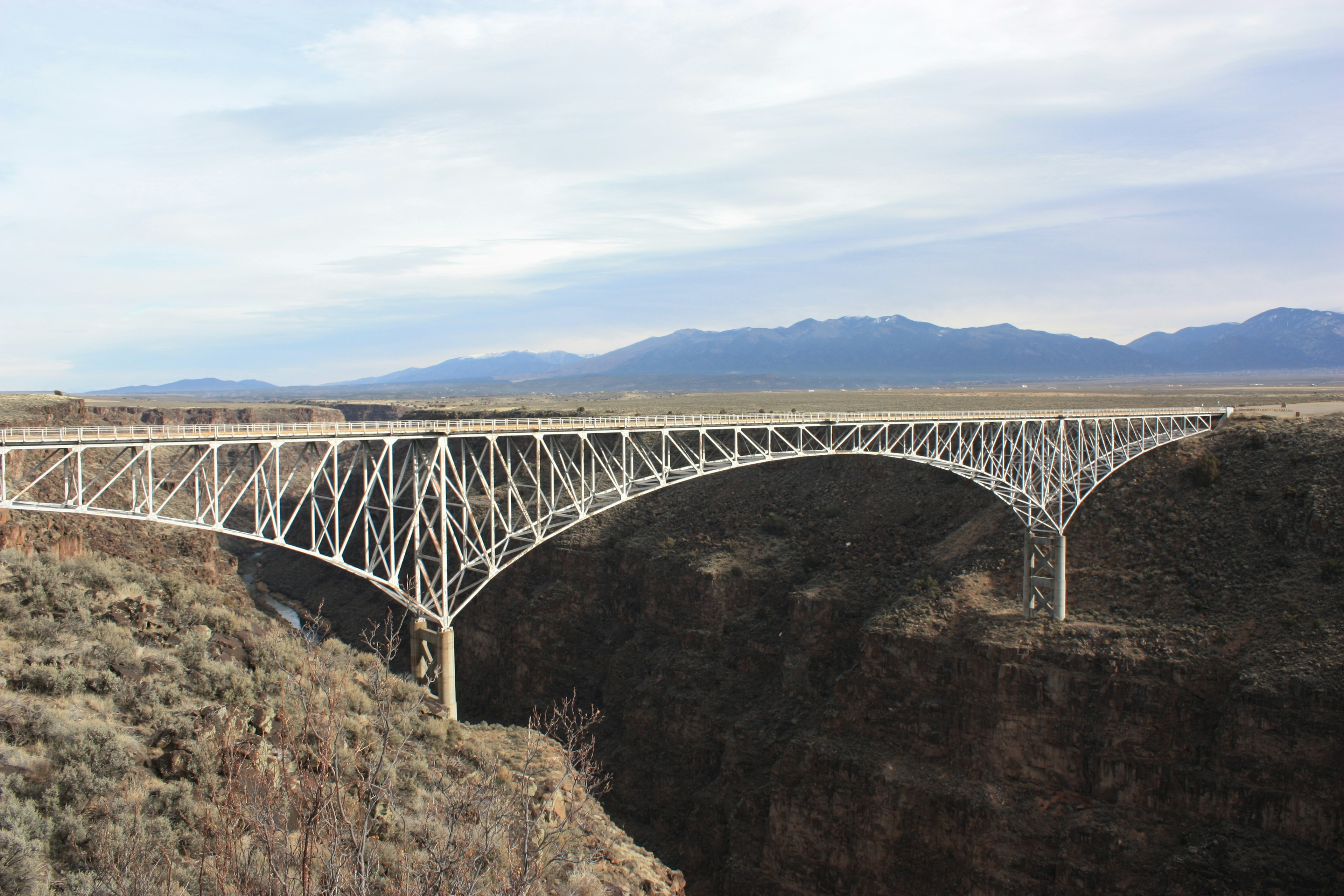 Puente de acero blanco que cruza un cañón con montañas al fondo