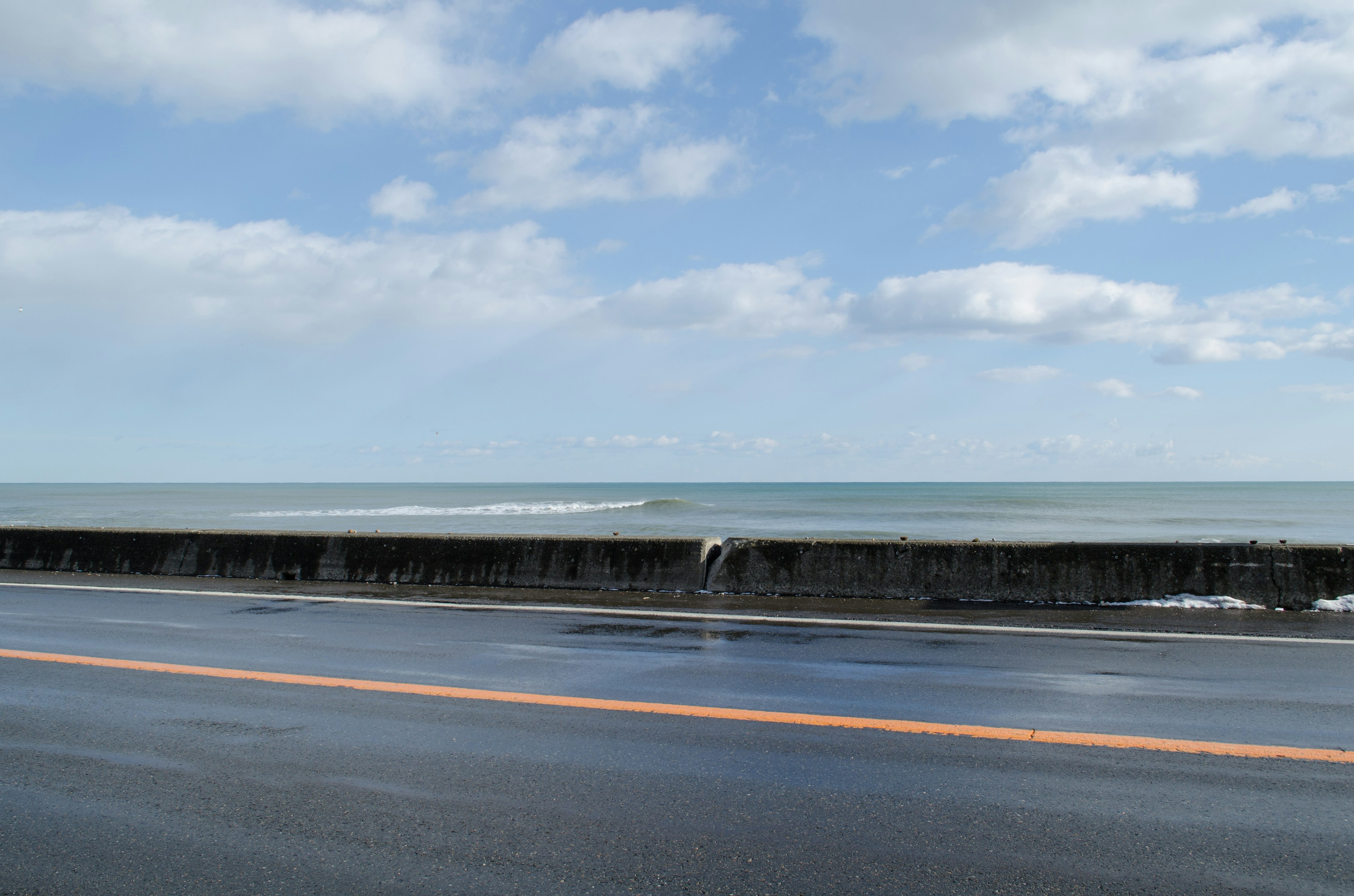 Scenic view of blue ocean and white clouds with a reflective road