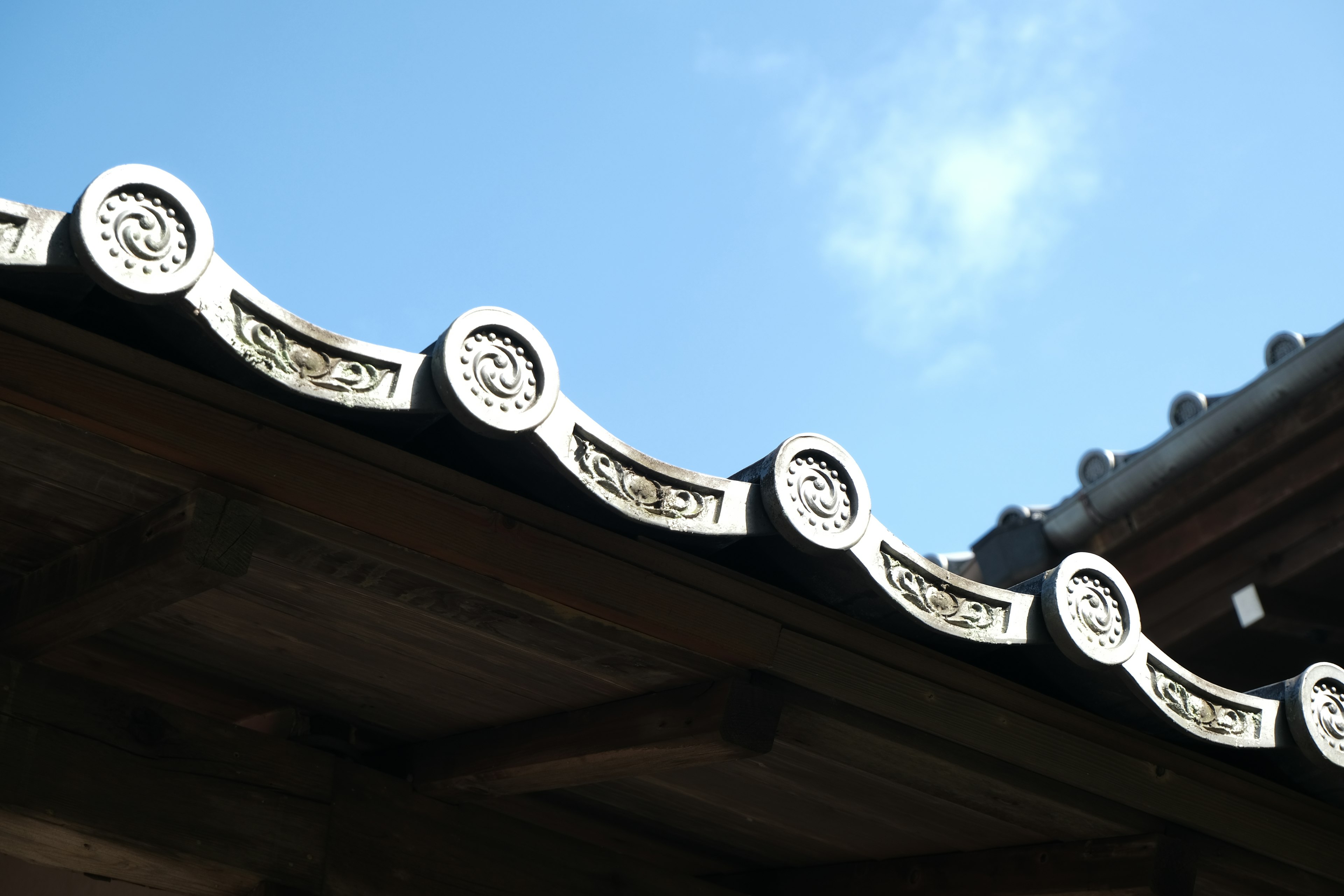 Traditional Japanese roof with decorative curves against a blue sky