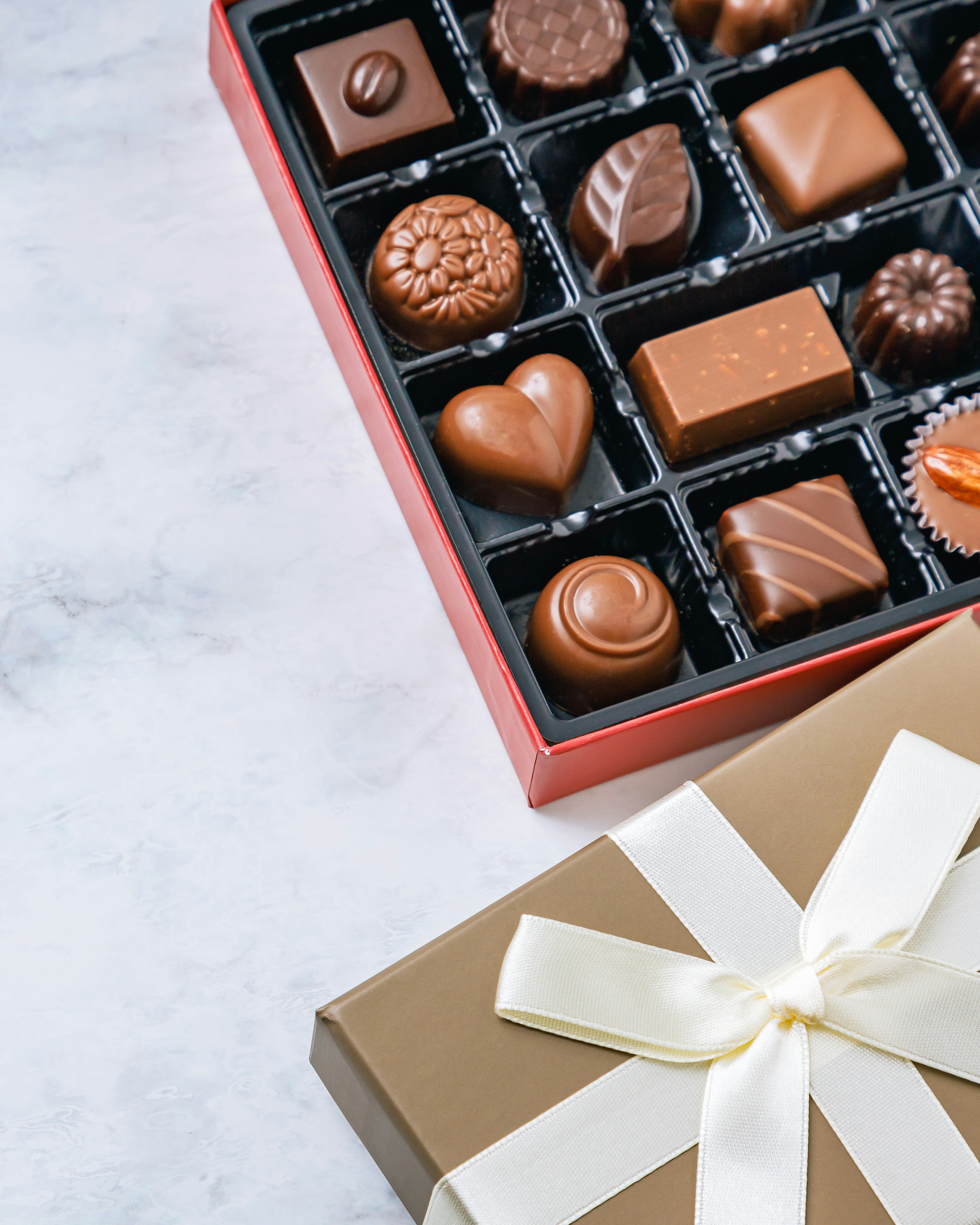 Une boîte rouge remplie de chocolats assortis et une boîte-cadeau dorée avec un ruban blanc