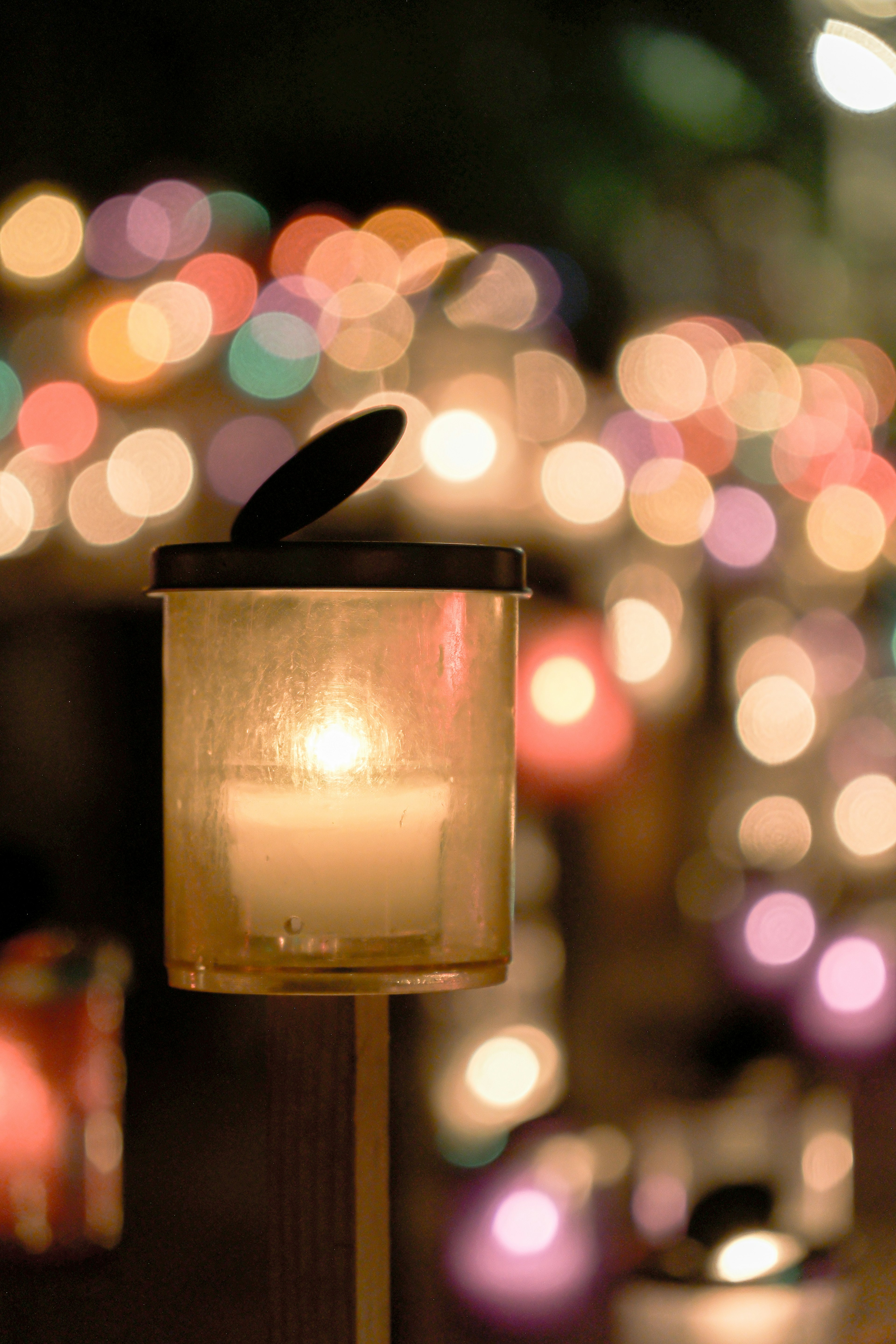 A glowing candle in a transparent lantern with a blurred colorful light background