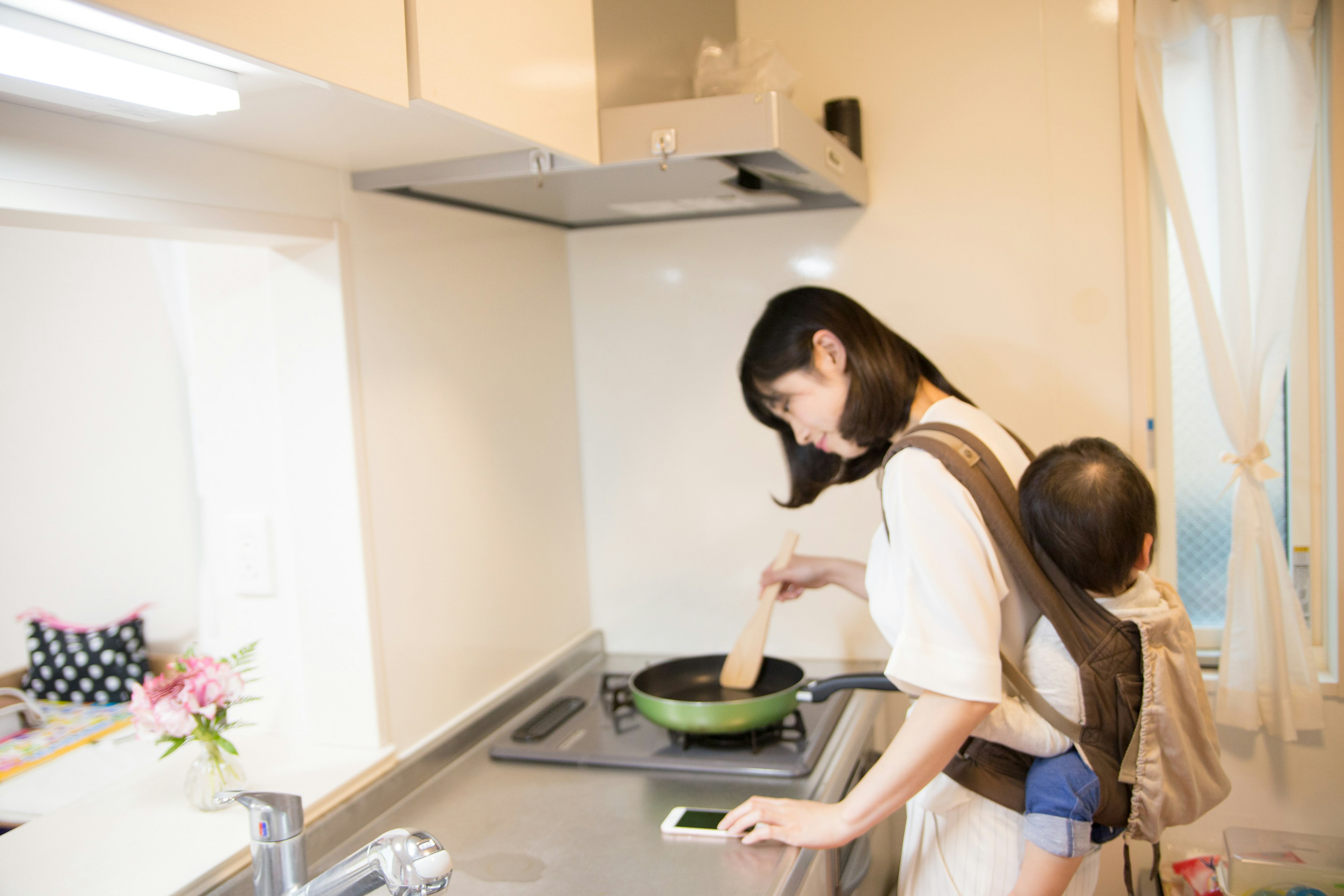 Una mujer cocinando en la cocina con un bebé en la espalda