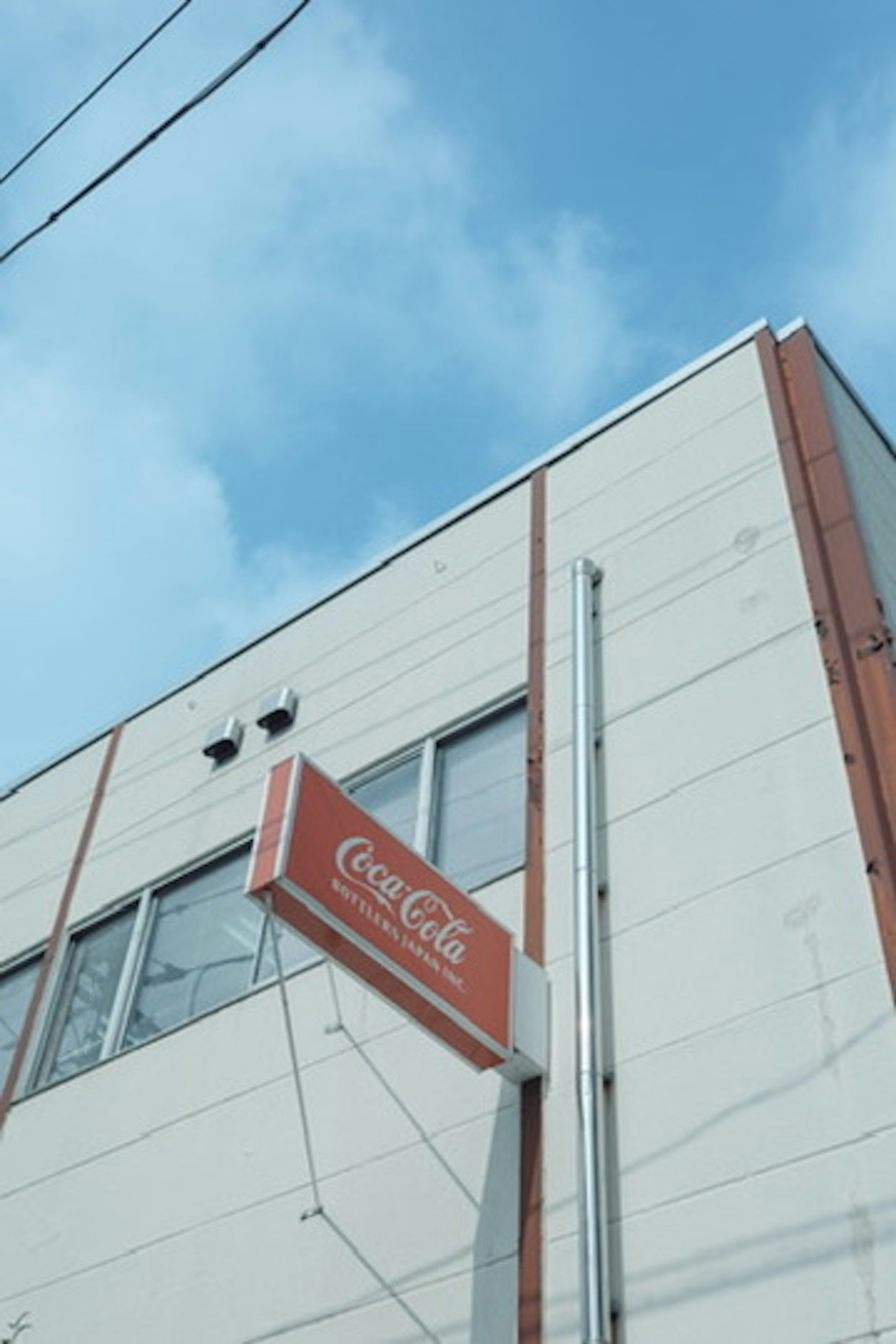 Building exterior featuring a Coca-Cola sign with blue sky and white clouds in the background