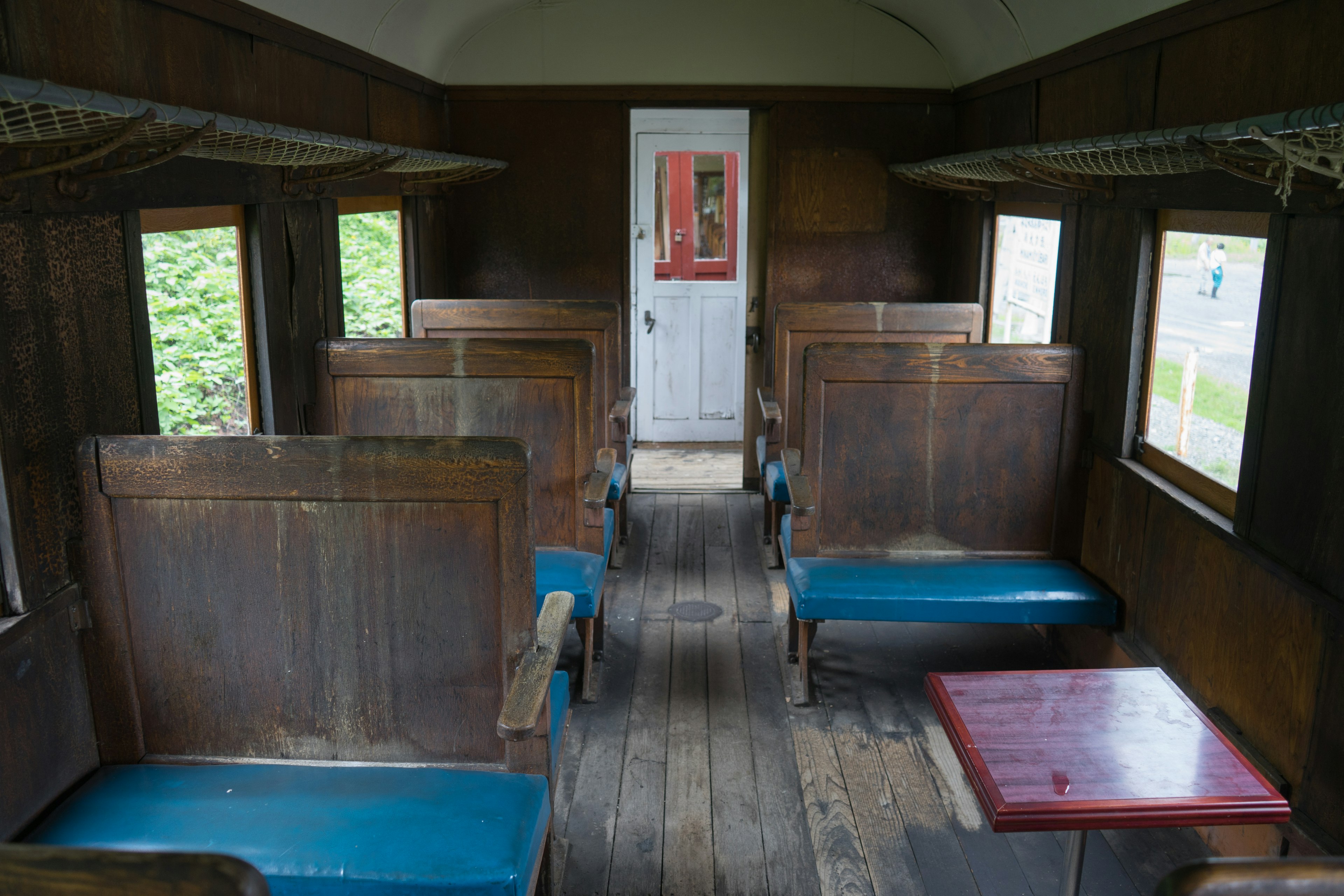 Intérieur d'un ancien wagon de train avec des murs en bois des sièges bleus une table centrale une porte rouge à l'arrière-plan