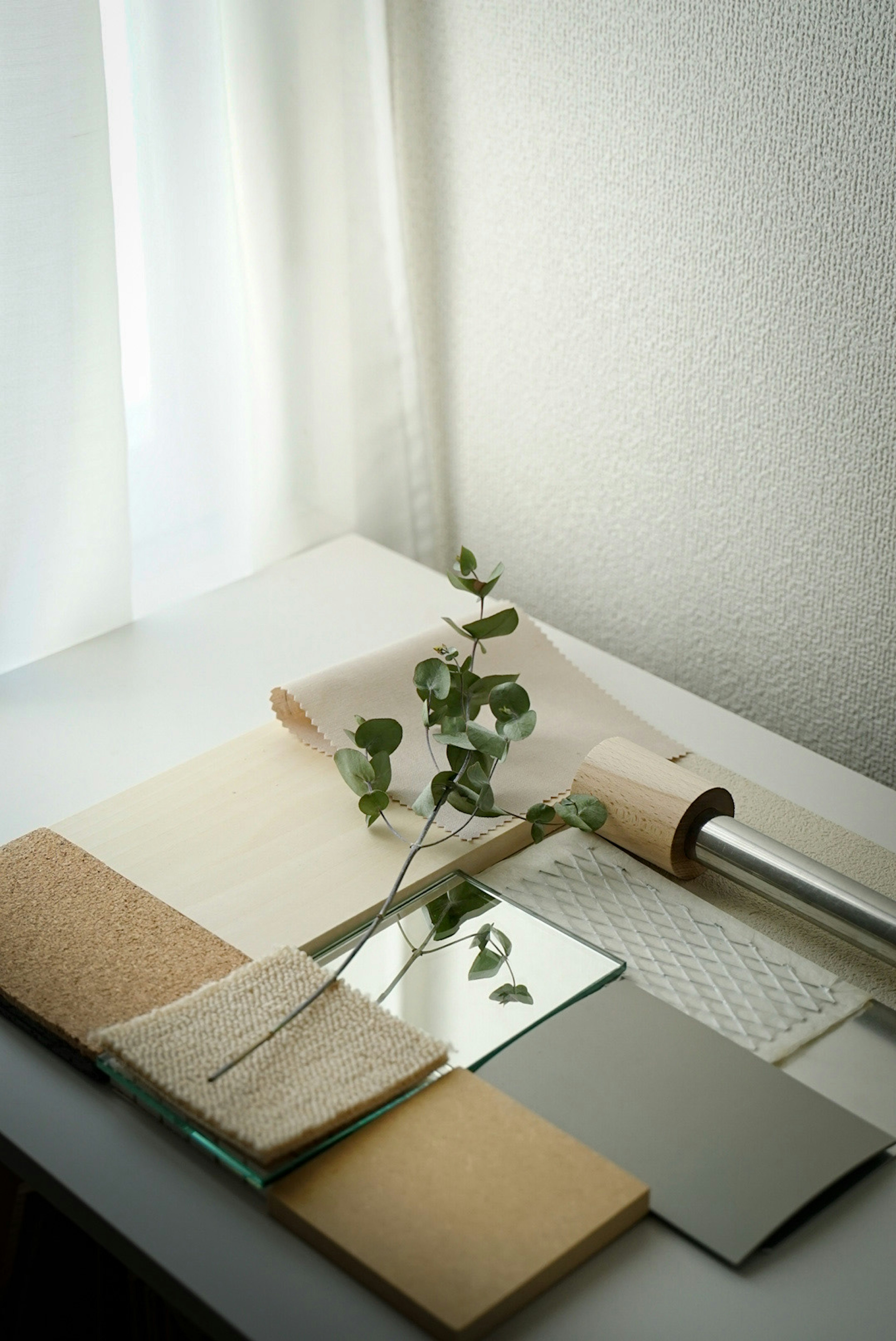 A collection of material samples and a eucalyptus branch on a table by a white curtain