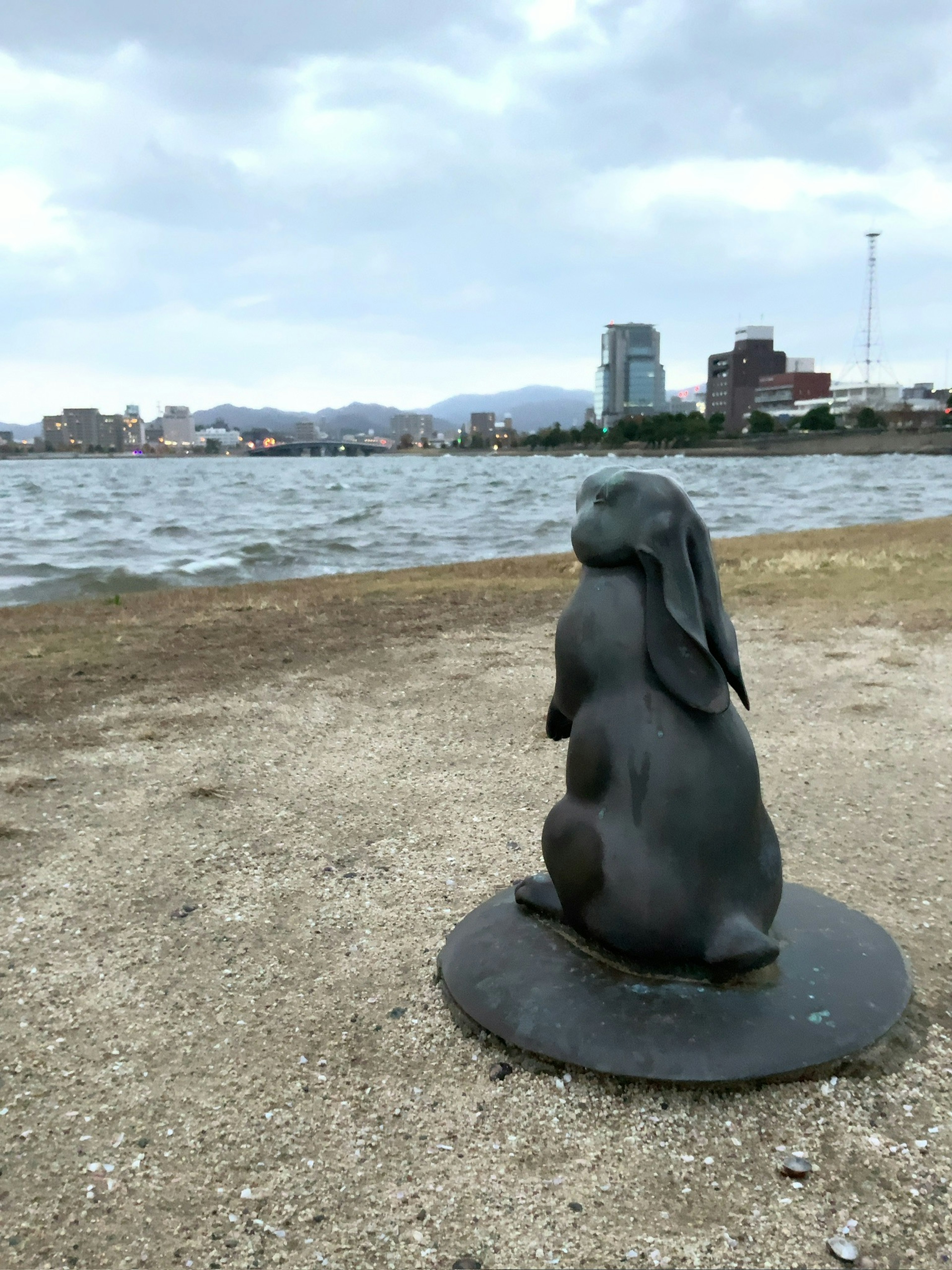 Bronze statue of a rabbit standing by the water urban skyline in the background