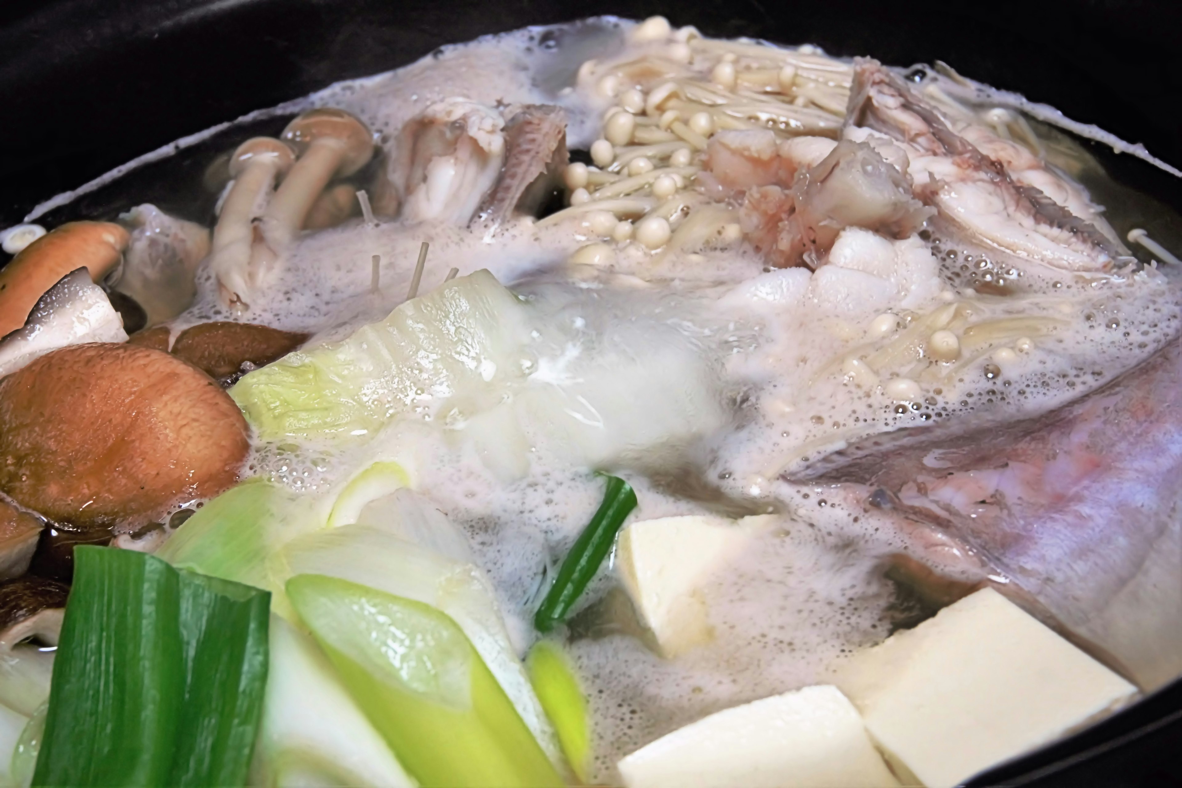 A hot pot dish with various ingredients simmering including mushrooms cabbage and tofu