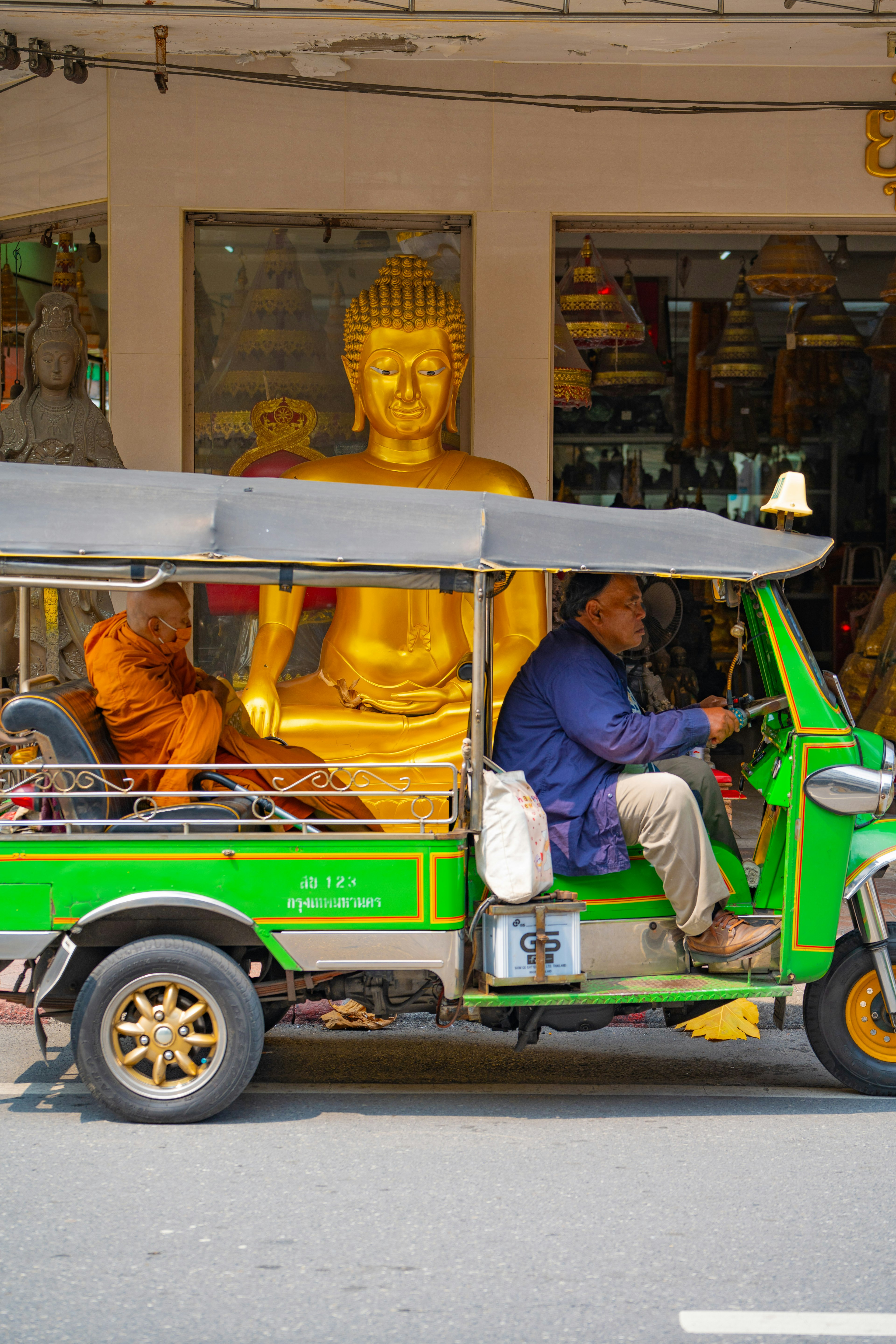 Sebuah tuk-tuk hijau melintas di depan patung Buddha emas