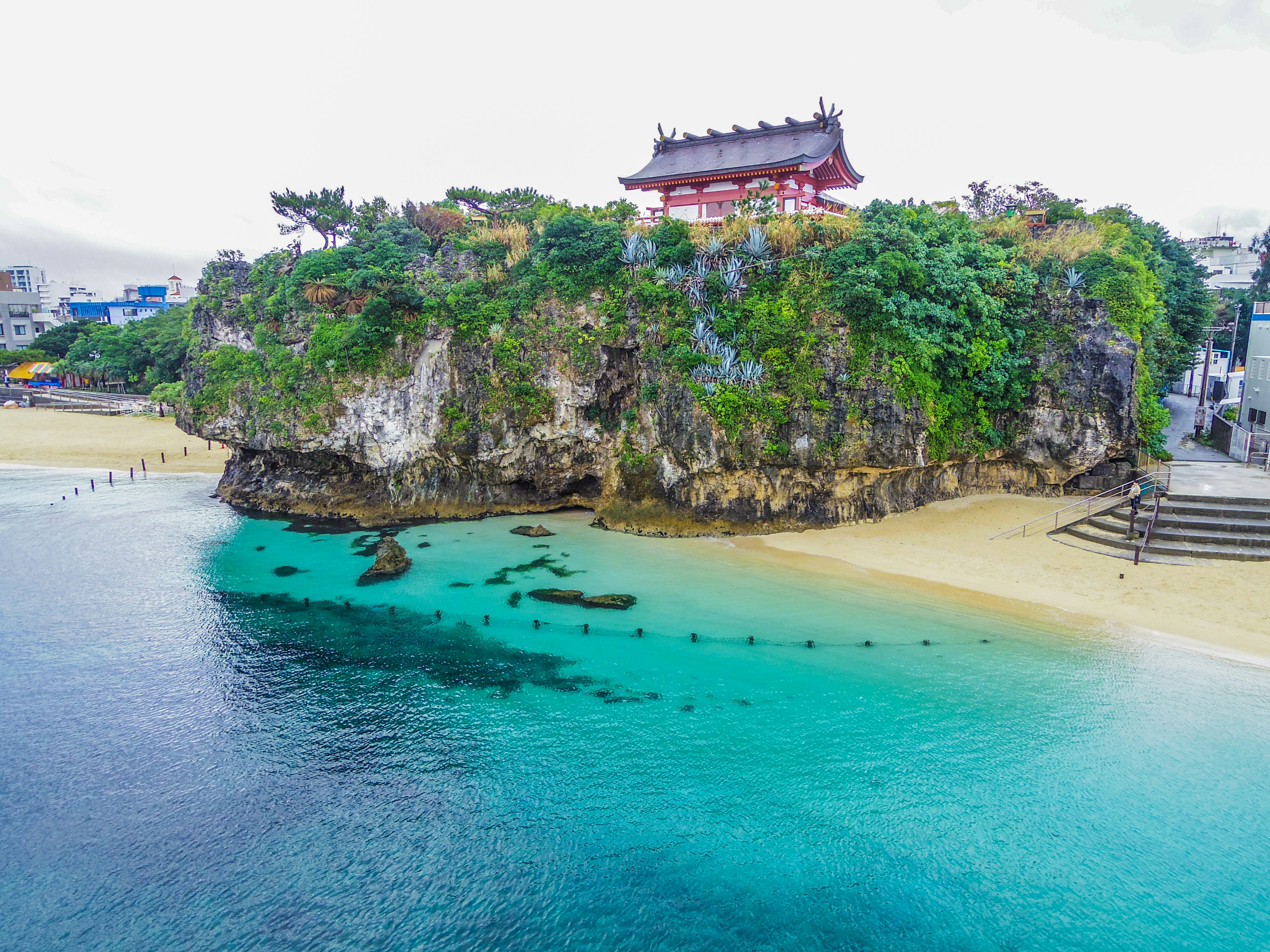 红色神社坐落在岩石上，周围是碧蓝的海水和沙滩