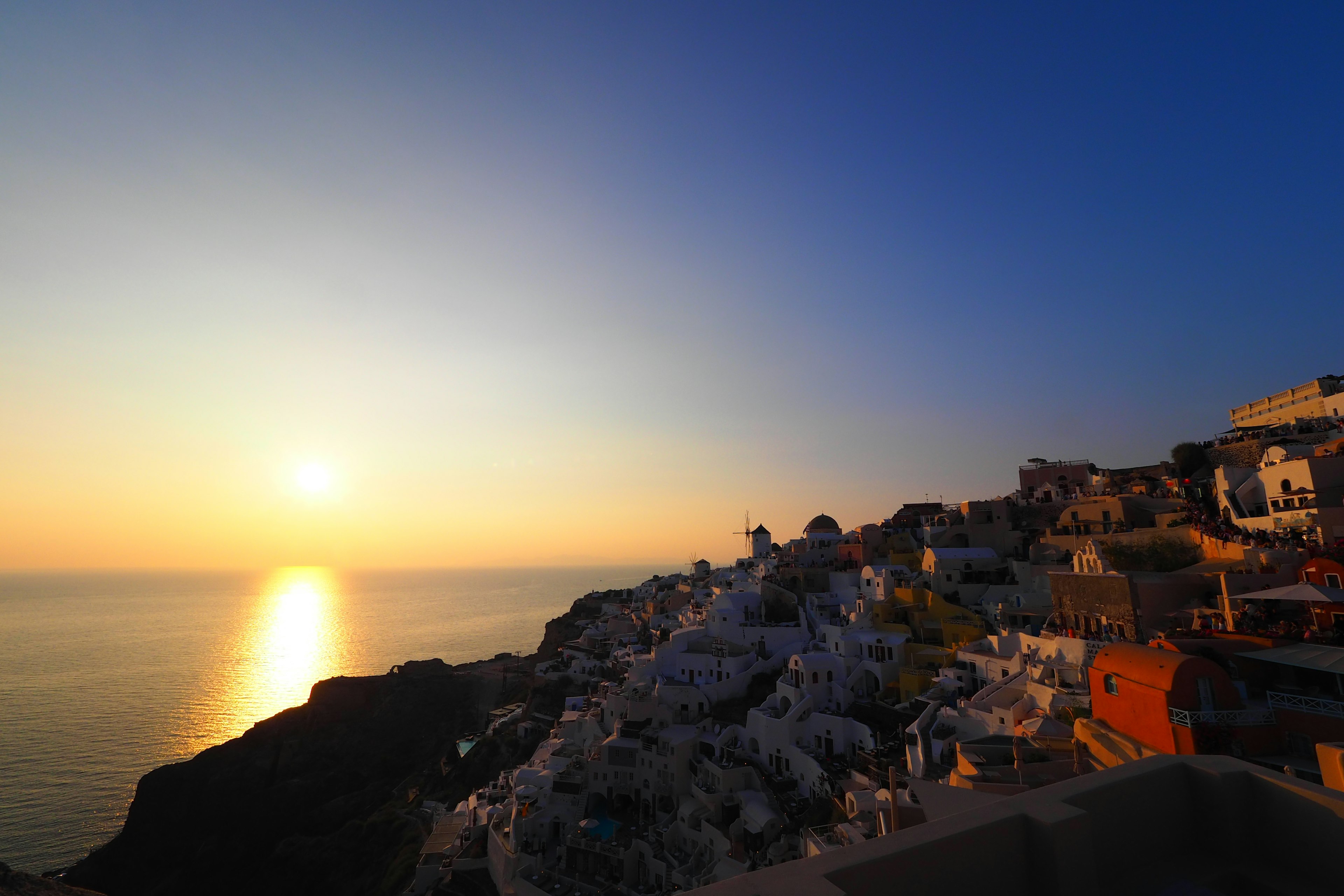 Pemandangan matahari terbenam yang indah di Santorini dengan bangunan putih di perbukitan