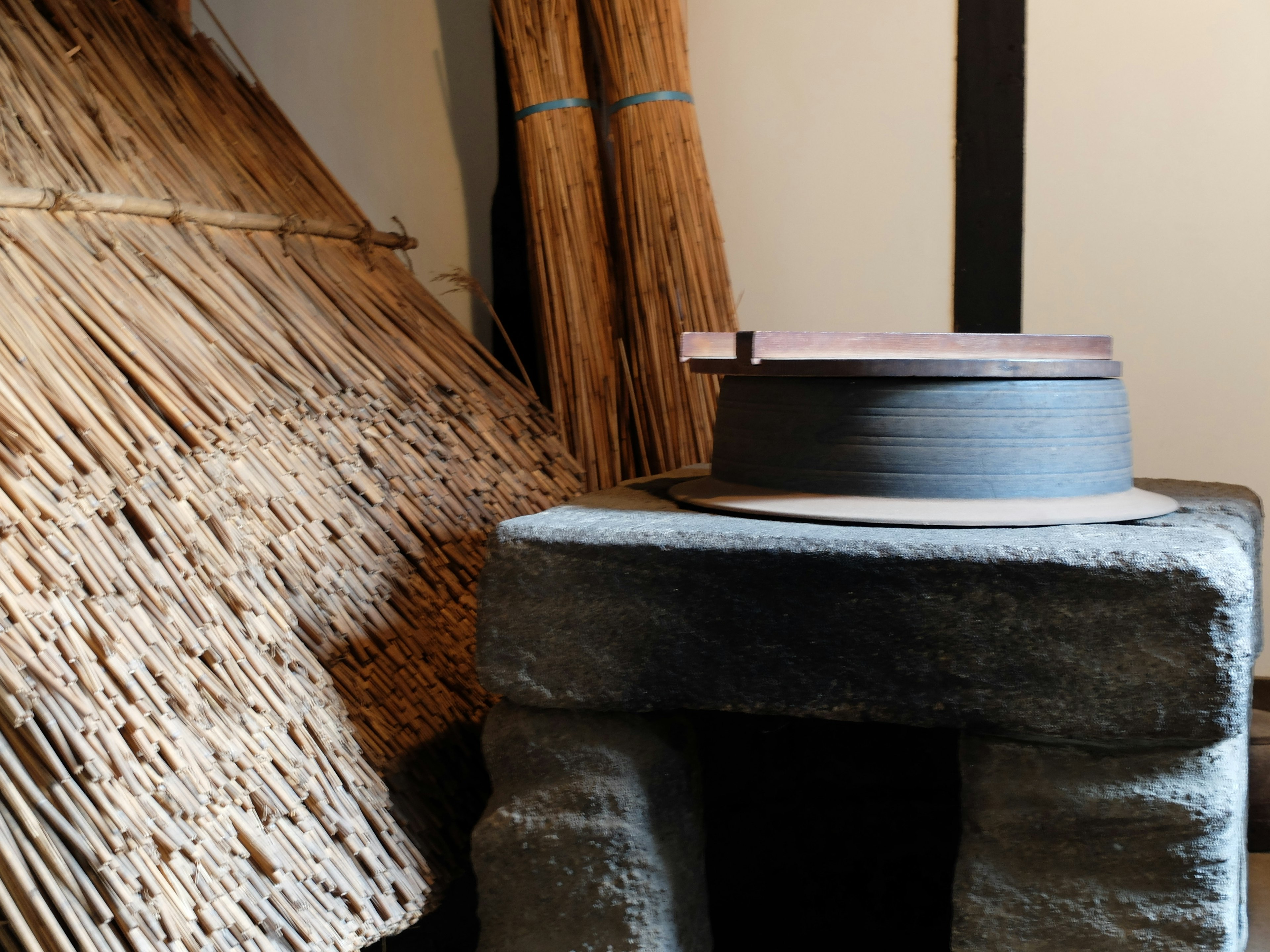 Interior de una casa japonesa tradicional con una plataforma de piedra y una olla de barro, montones de paja al fondo