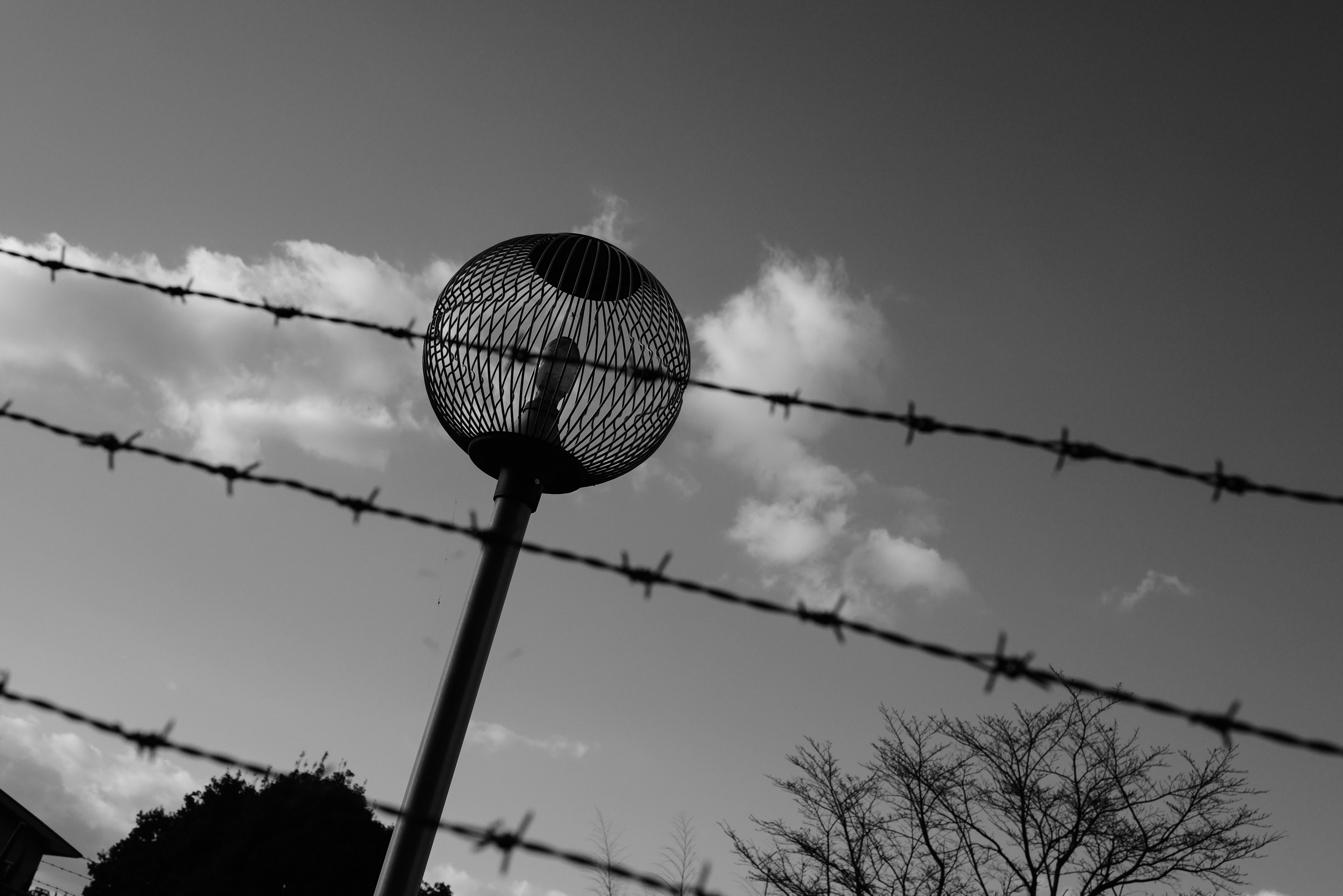 Silhouette eines Stacheldrahtzauns mit einer Sicherheitskugel vor einem bewölkten Himmel