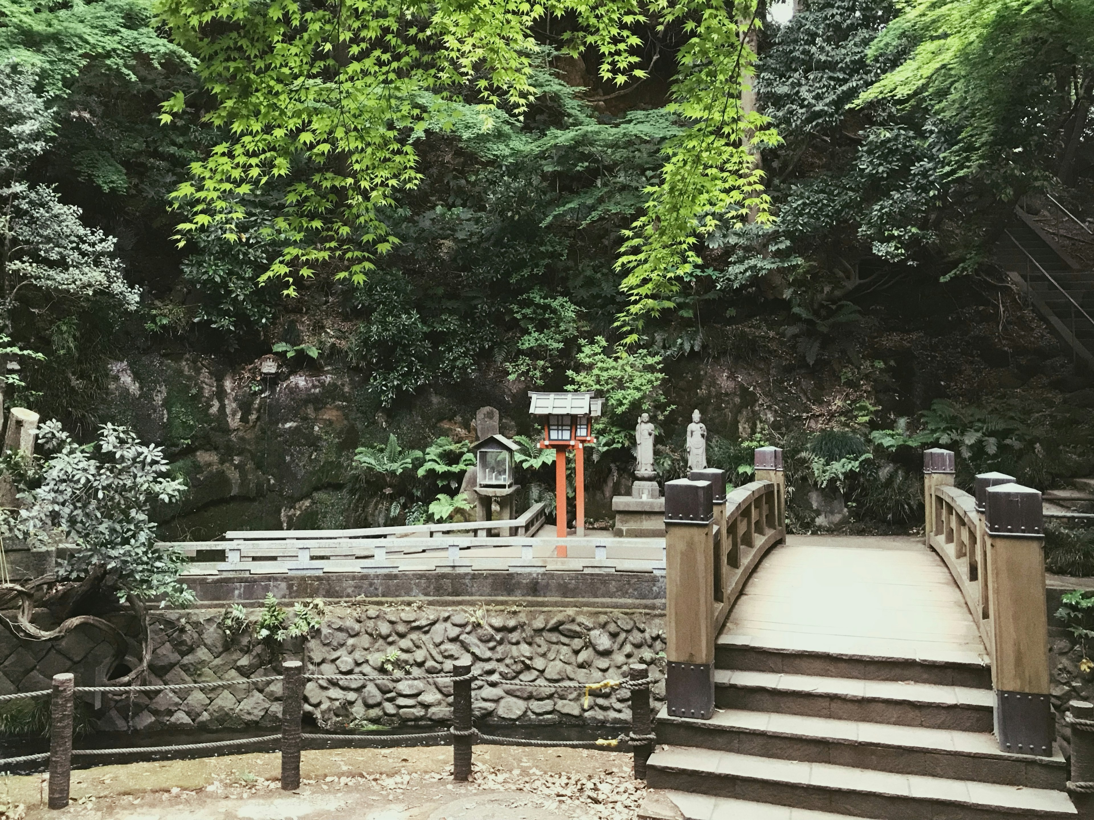 A serene scene featuring a wooden bridge and stone statues surrounded by lush greenery