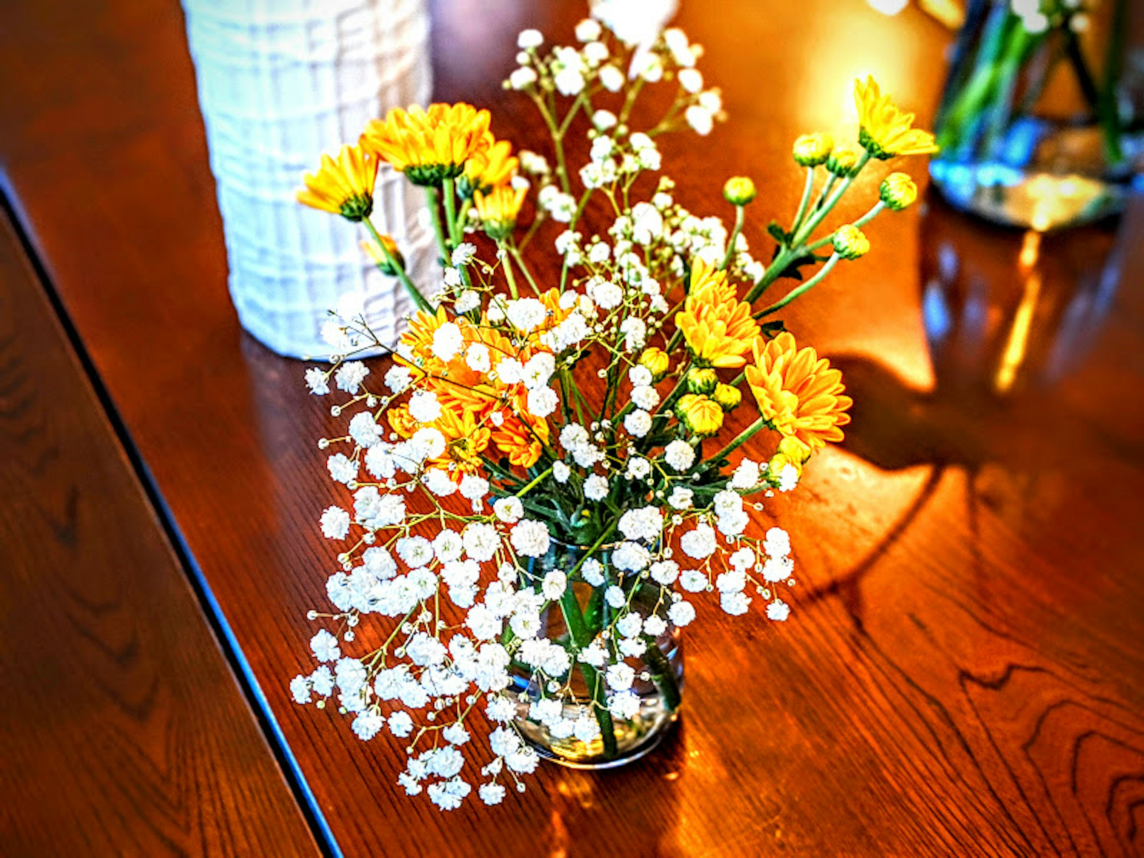 A vase with yellow flowers and white baby's breath on a wooden table