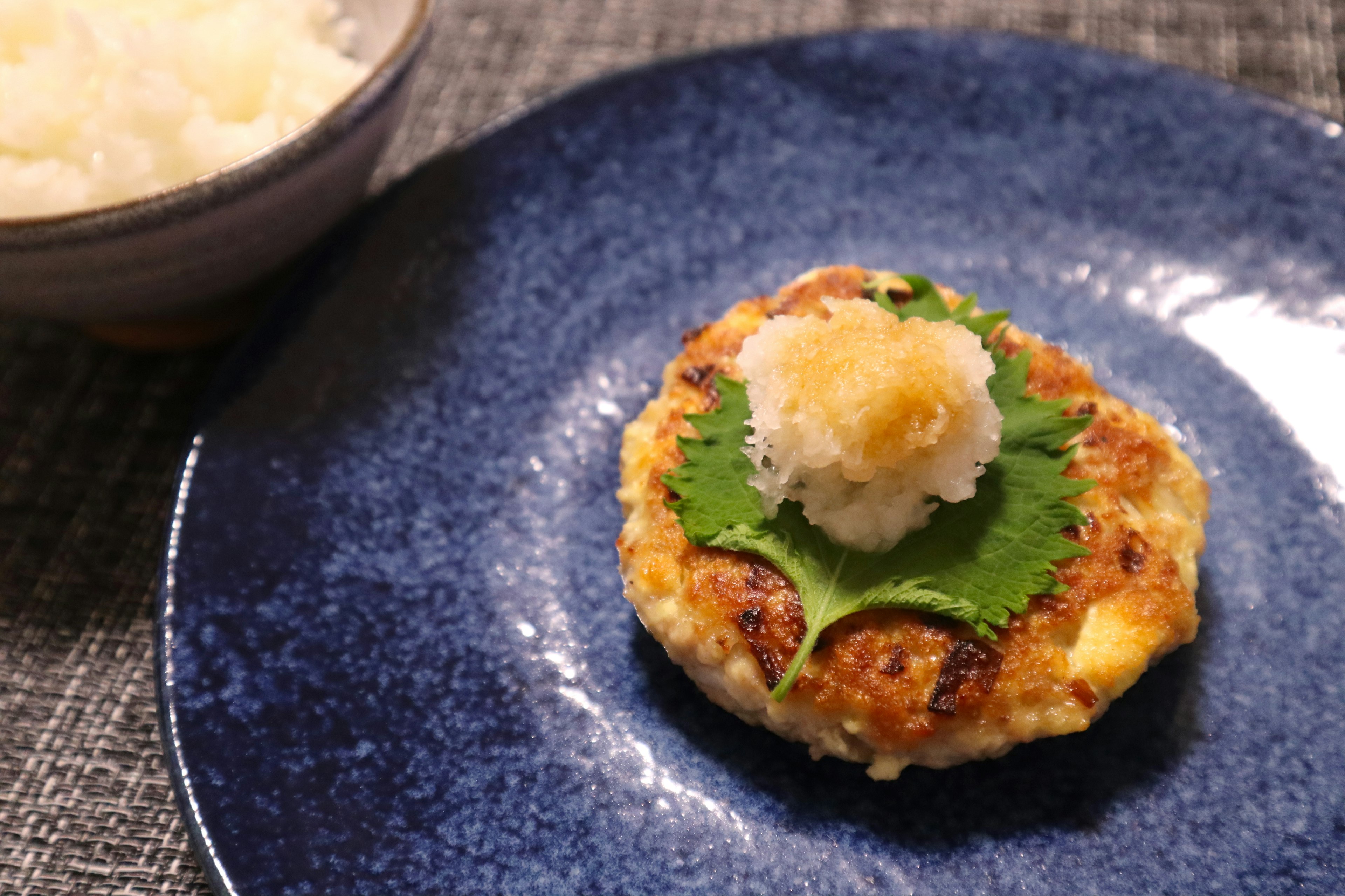 Gegrillter Fischpatty mit geriebenem Daikon und Shisoblatt auf einem blauen Teller