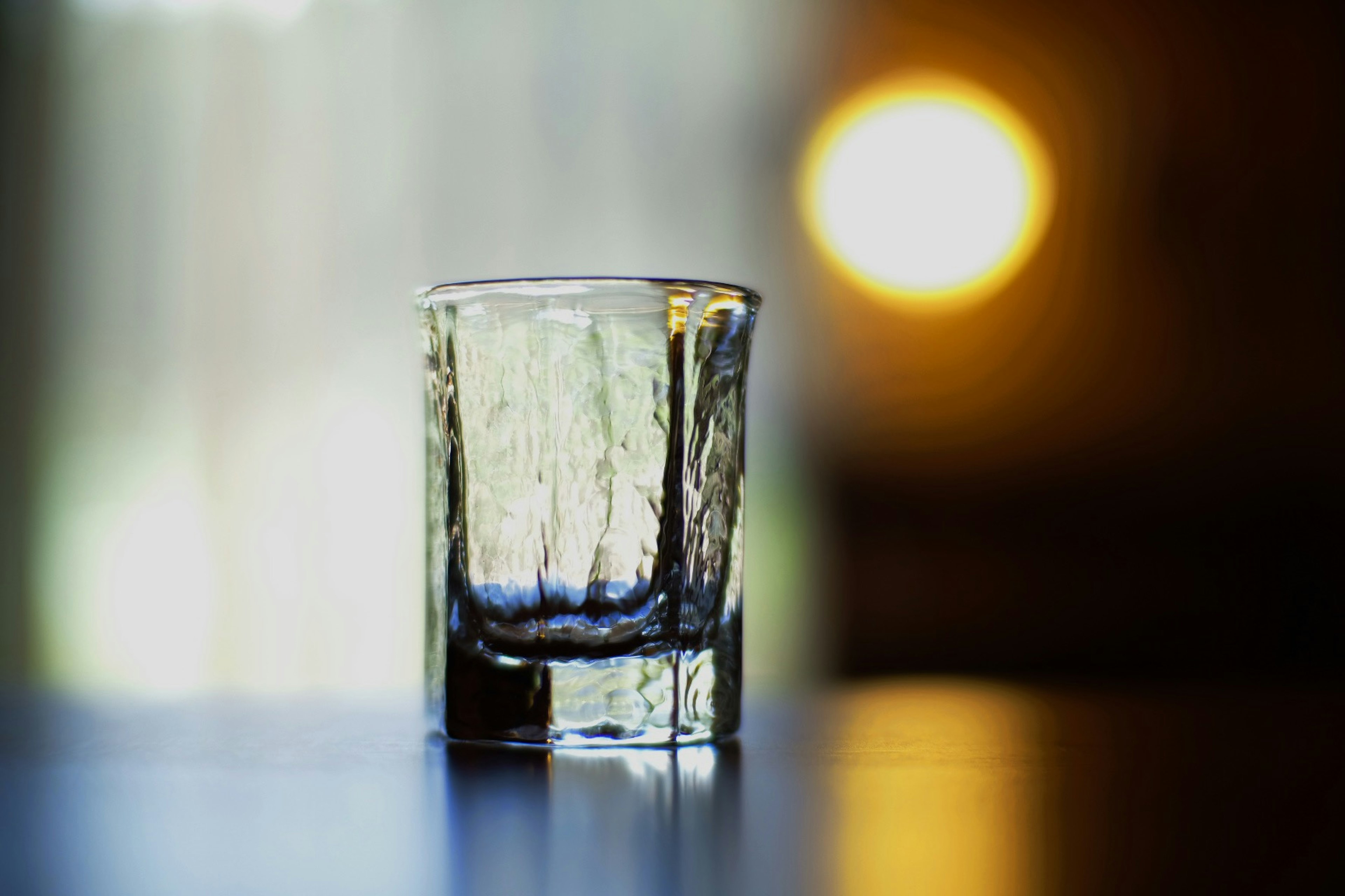 A clear glass placed on a table with a blurred light in the background