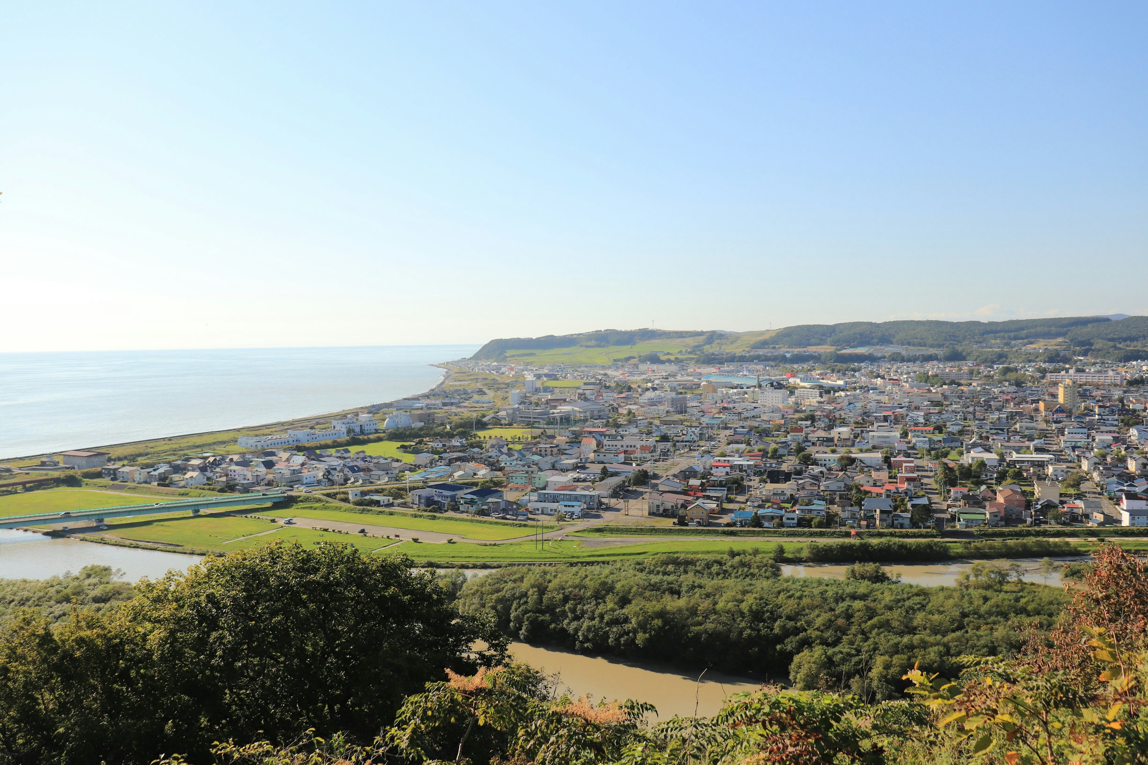 Scenic view of a coastal town with blue sky and green fields