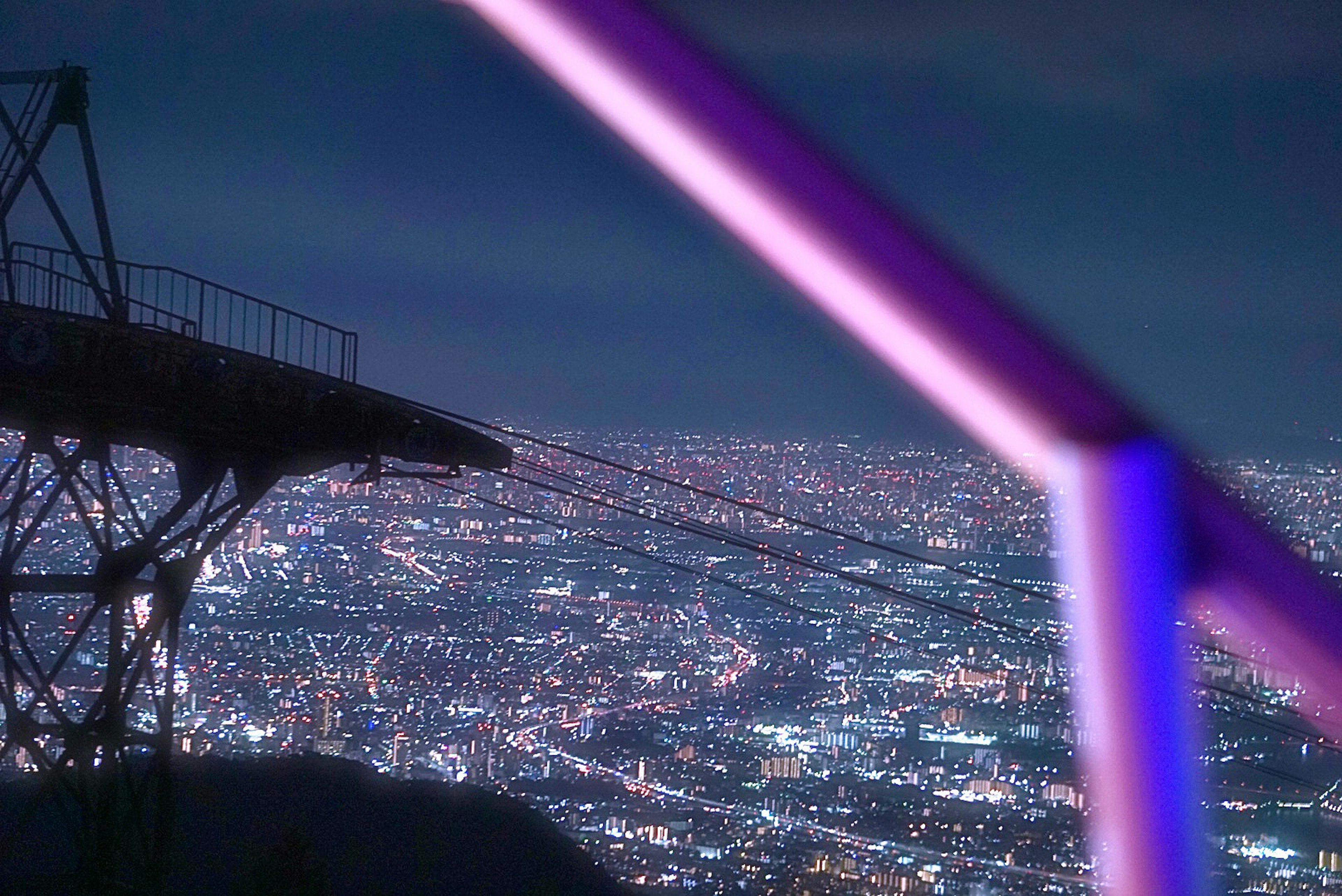 Partial view of a structure with purple lighting against a night cityscape