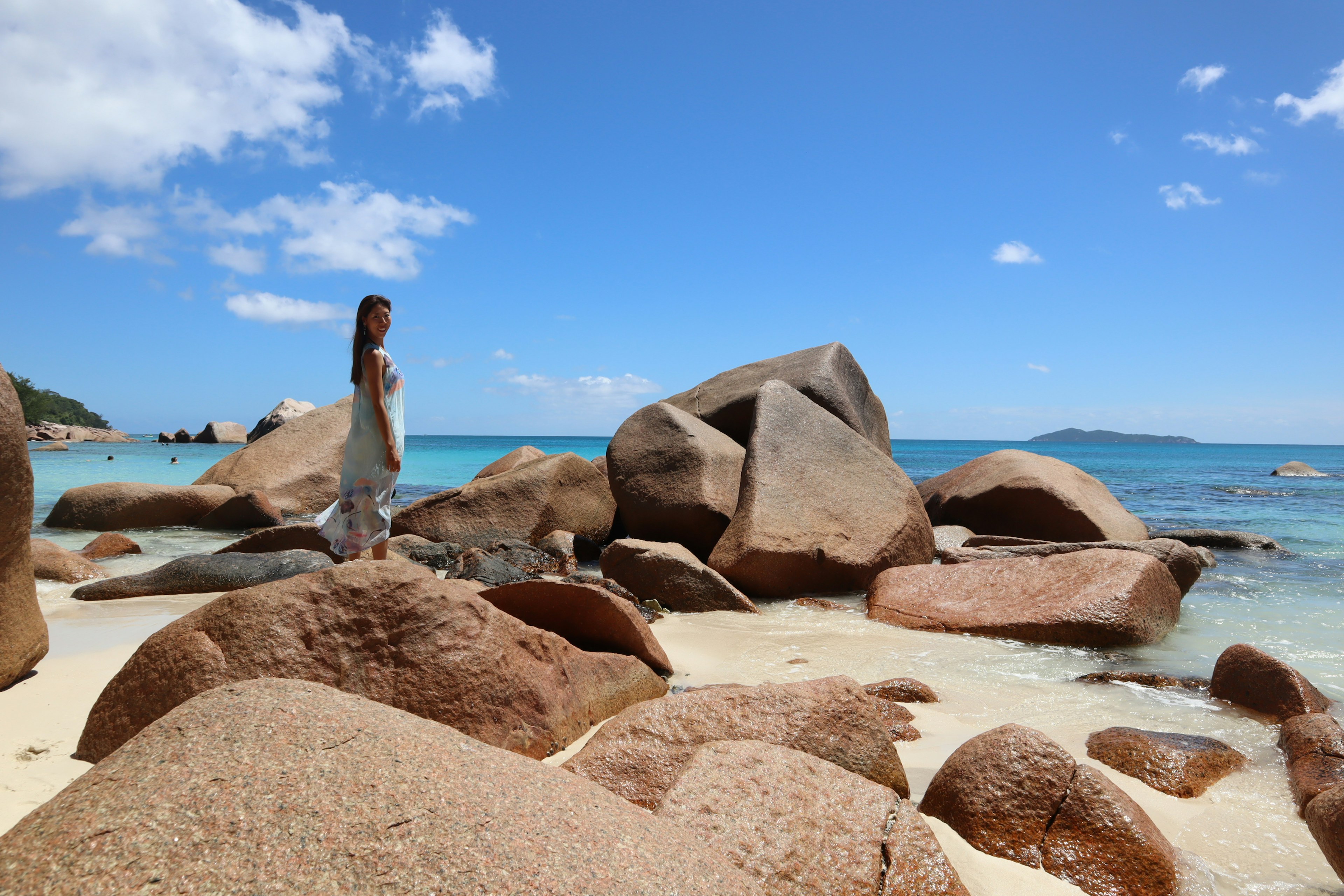 A woman standing on a beach surrounded by large rocks and clear blue water