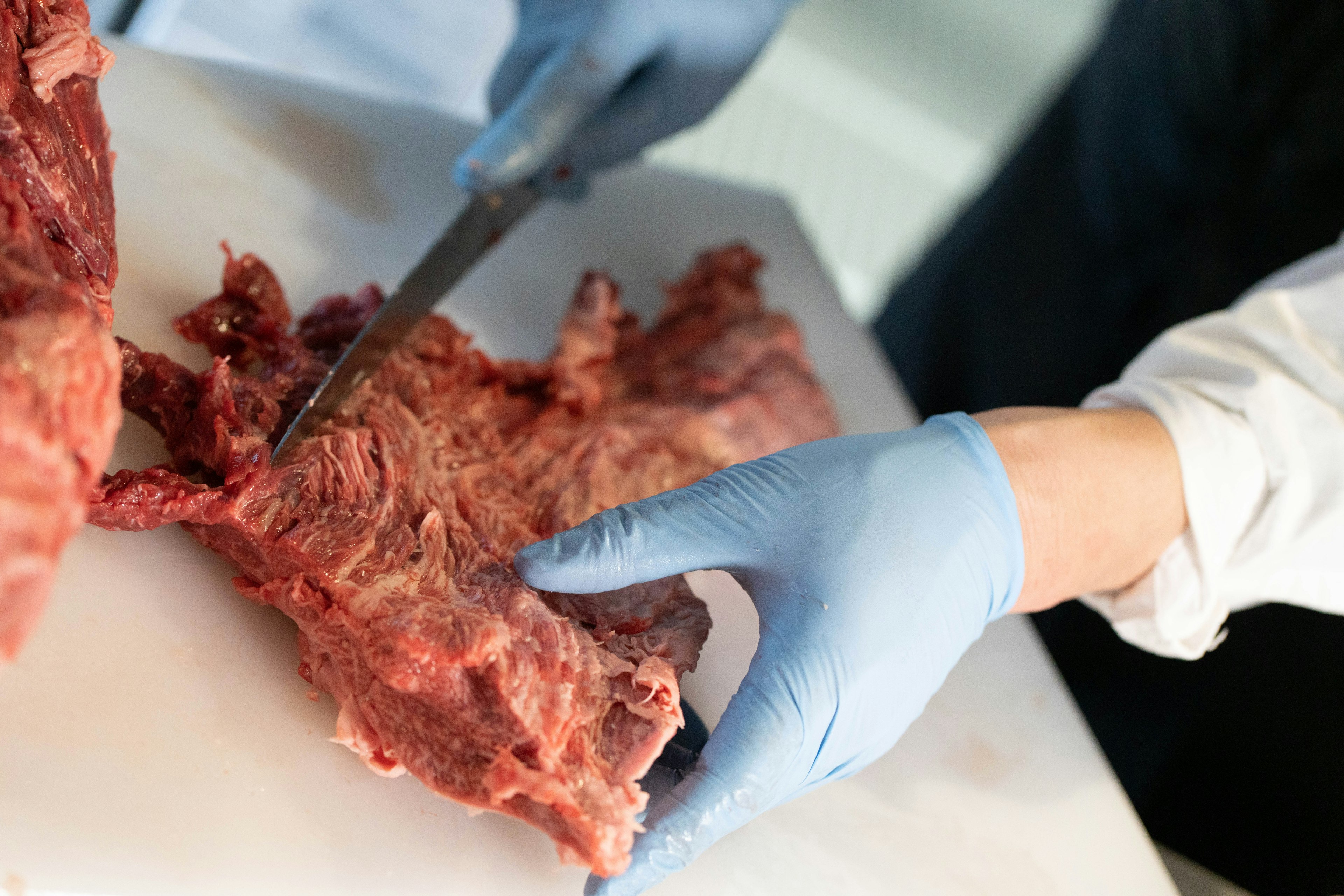 Primo piano di mani che usano un coltello per tagliare carne cruda