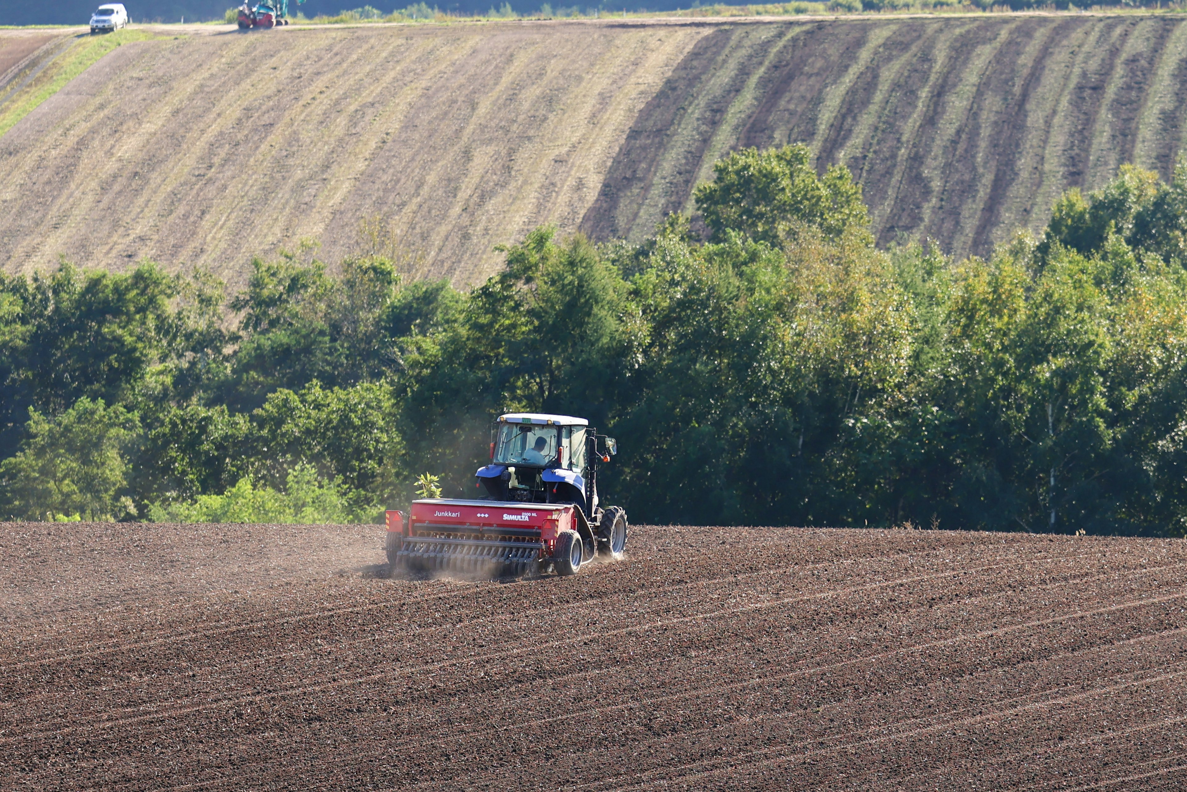 Agrarischer Traktor, der den Boden in einem Feld mit grünen Bäumen im Hintergrund pflügt