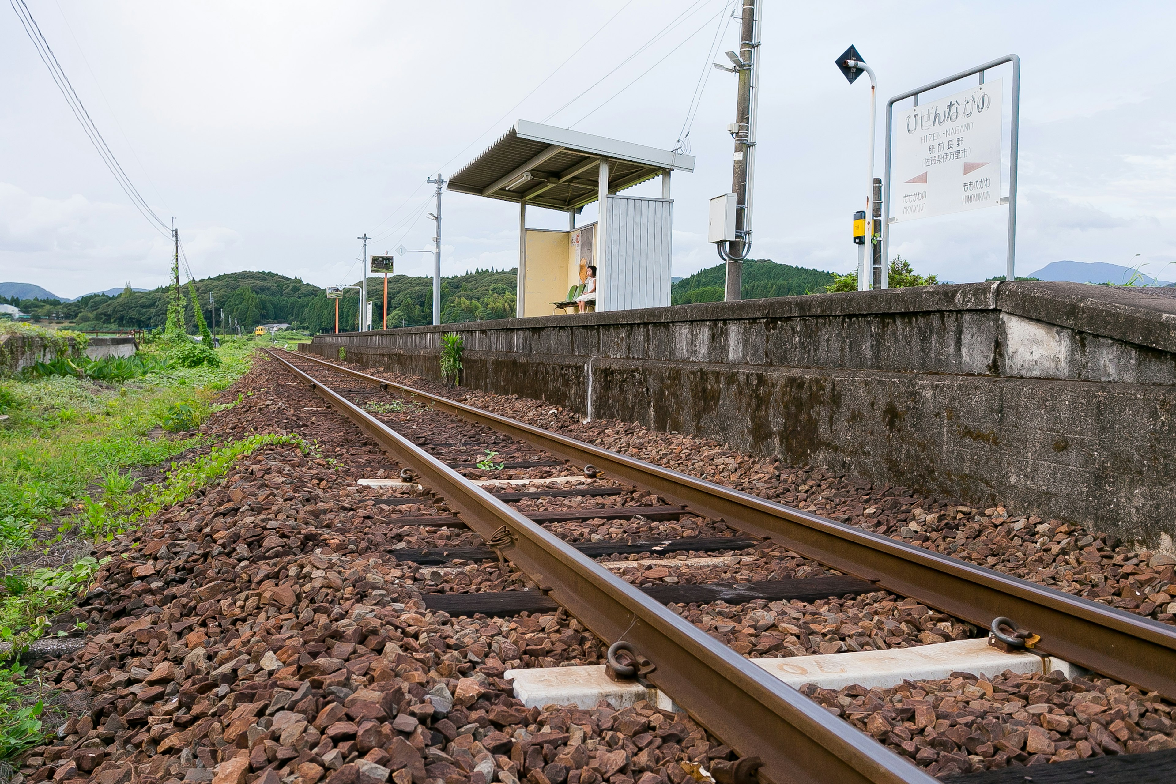 Vías de tren con una pequeña estación rodeada de vegetación y colinas