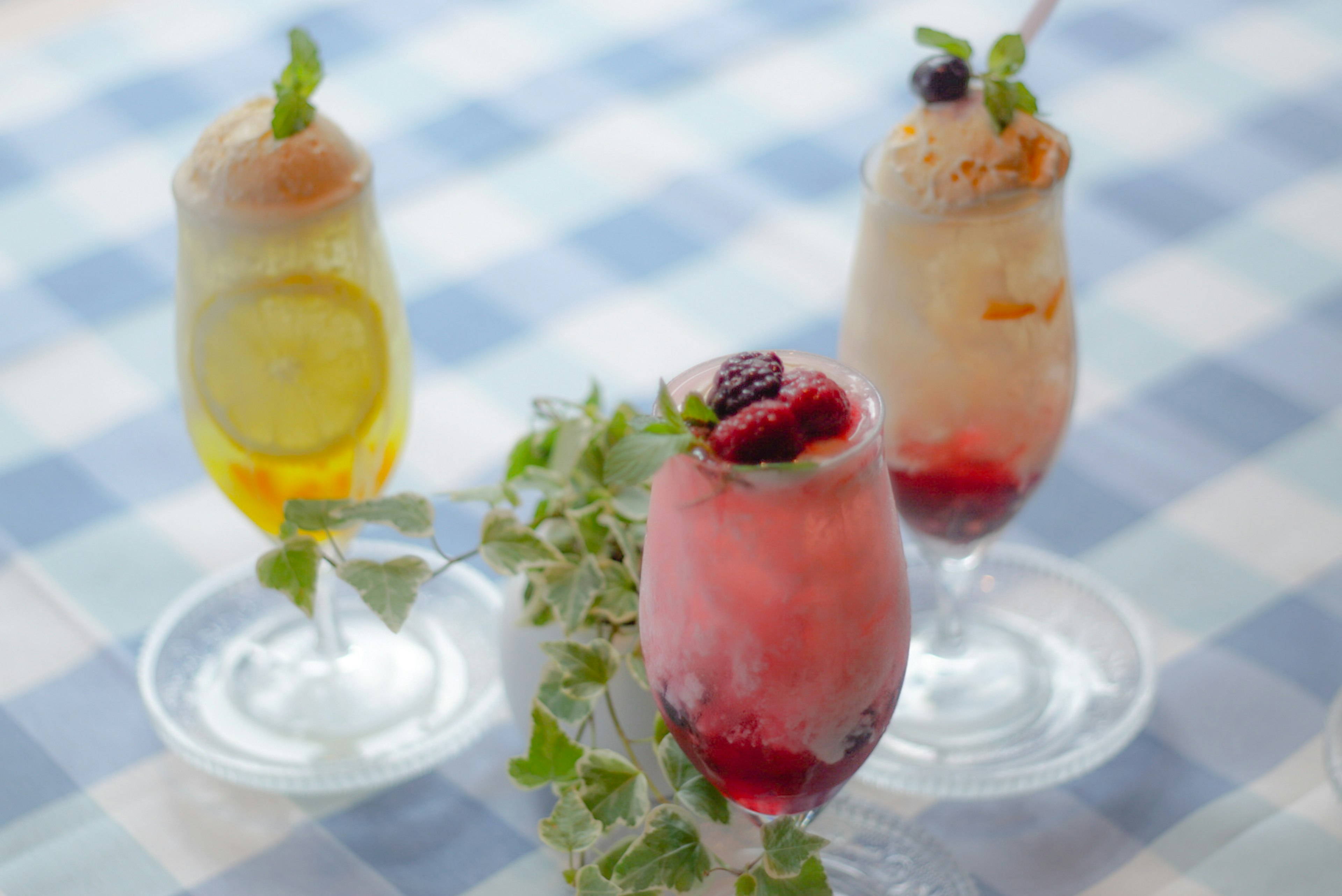 Trois boissons colorées dans des verres élégants sur une nappe à carreaux