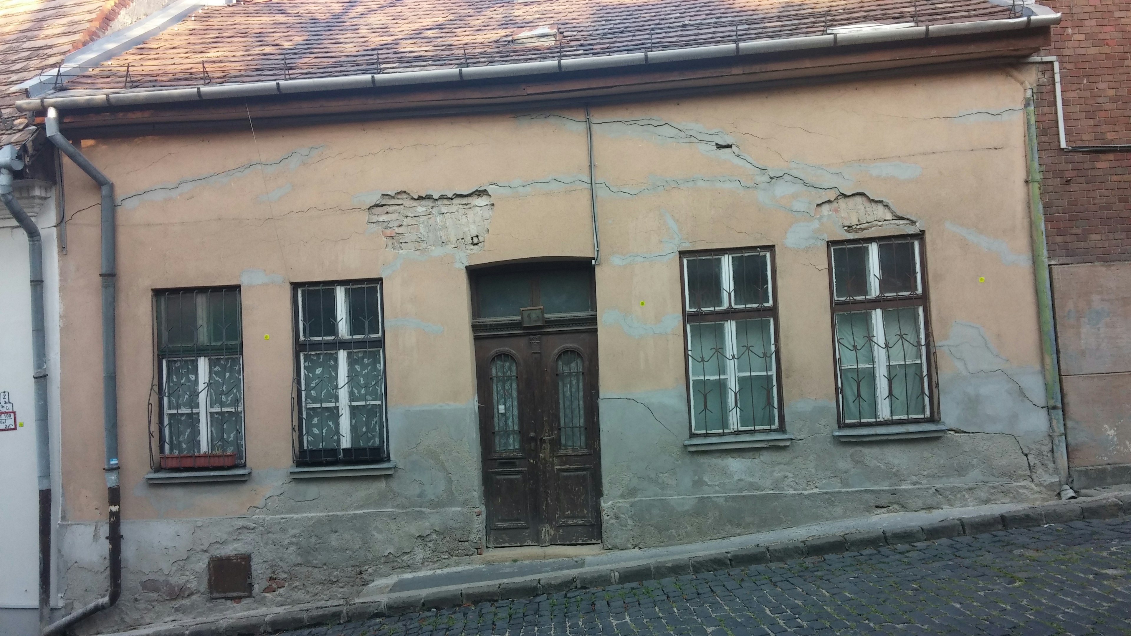 Außenansicht eines alten Hauses mit rissigen Wänden und markanten Fenstern