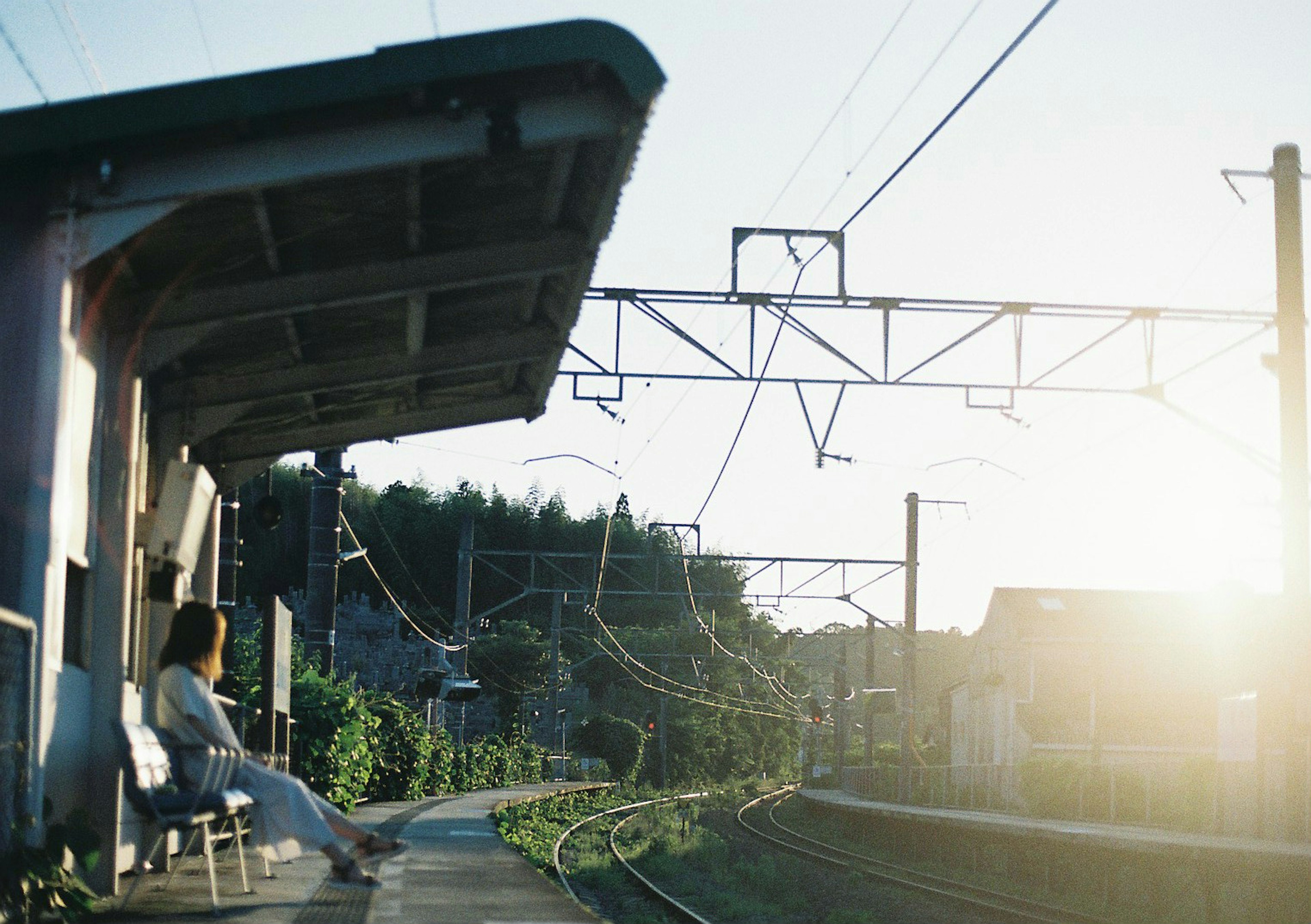 夕日の中の駅のベンチに座る女性と線路