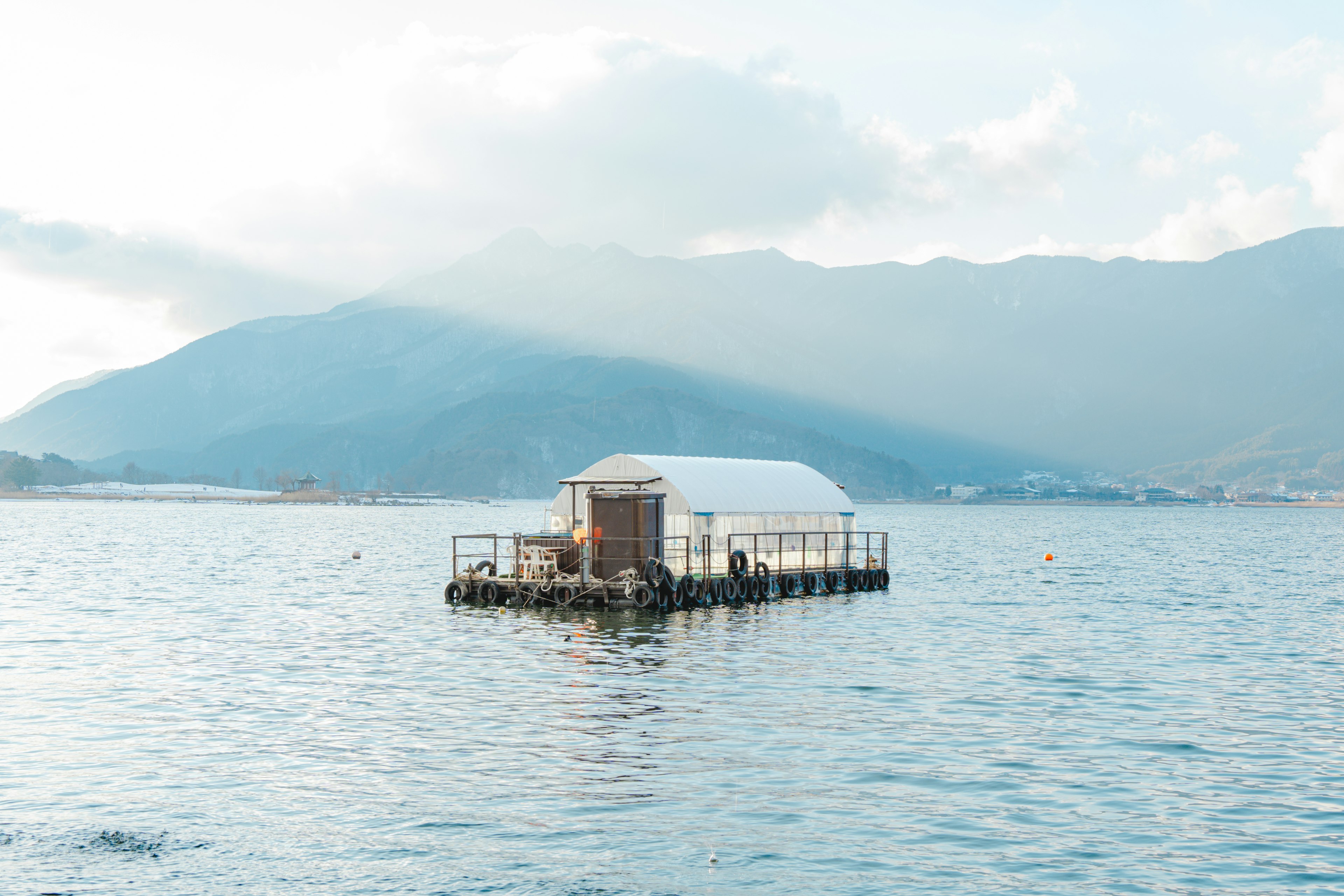 水面に浮かぶ白い小屋と山々の背景