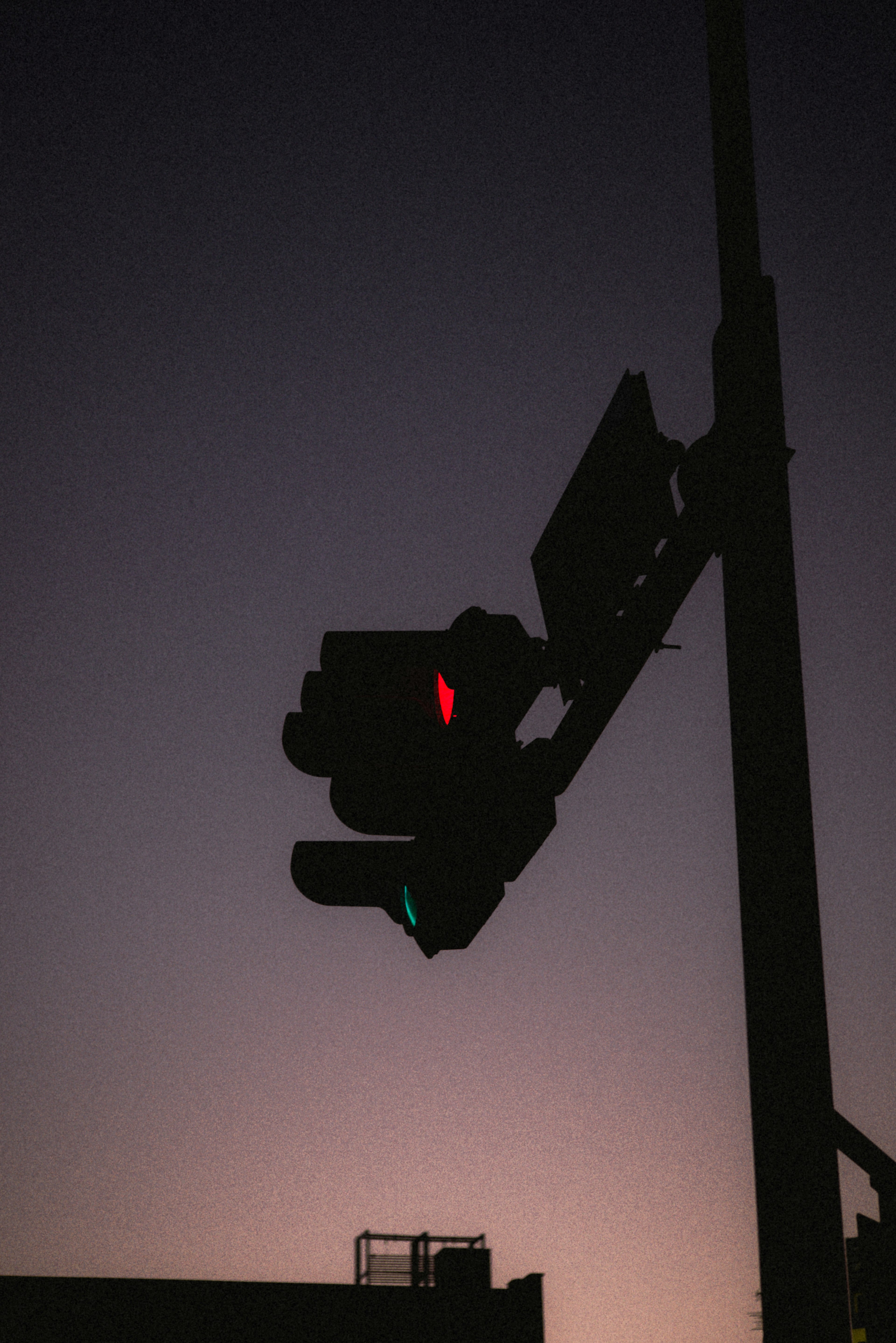 Silhouette of a traffic light at dusk showing red and green lights