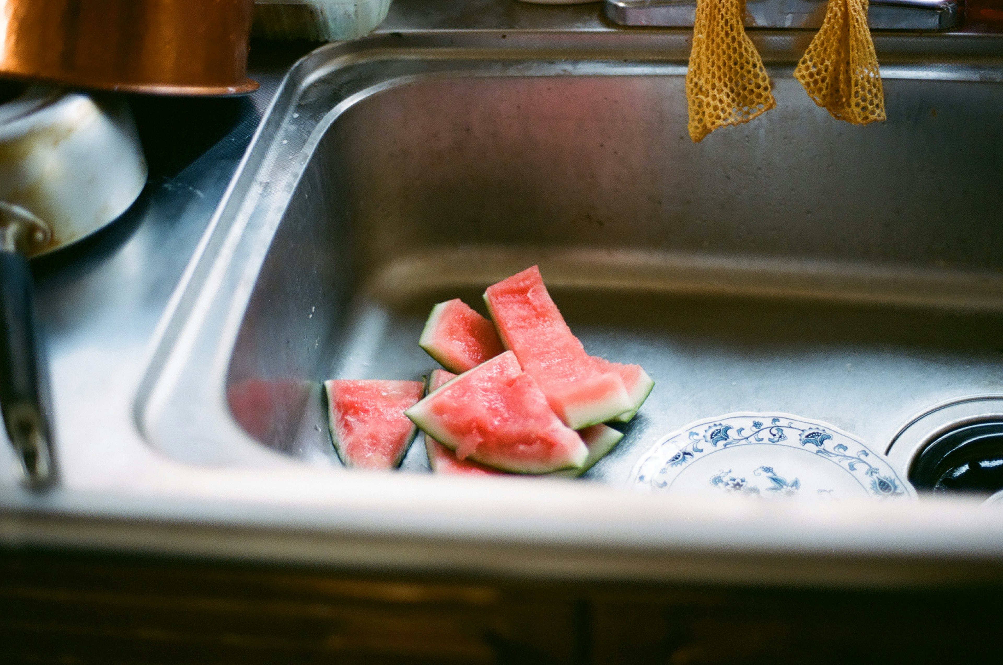 Slices of watermelon in a kitchen sink with a plate