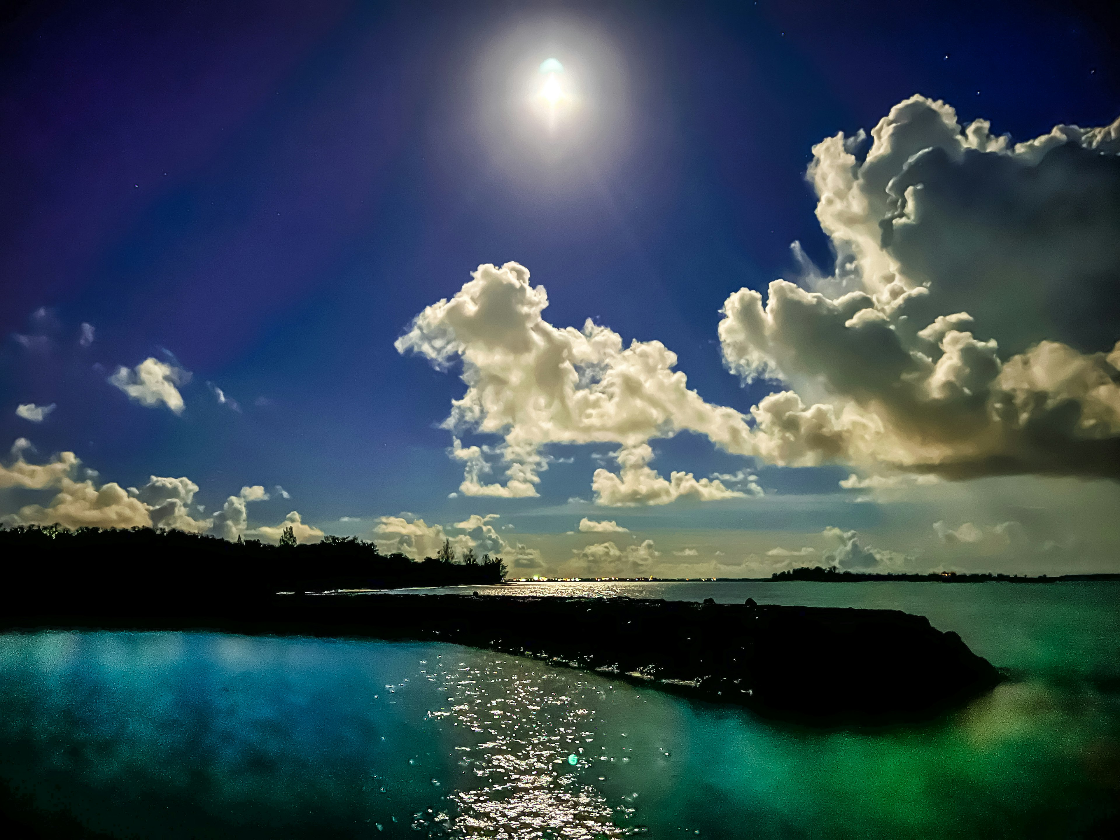 Eine ruhige Nachtszene mit einem hellen Mond, der sich auf ruhigem Wasser und flauschigen Wolken spiegelt