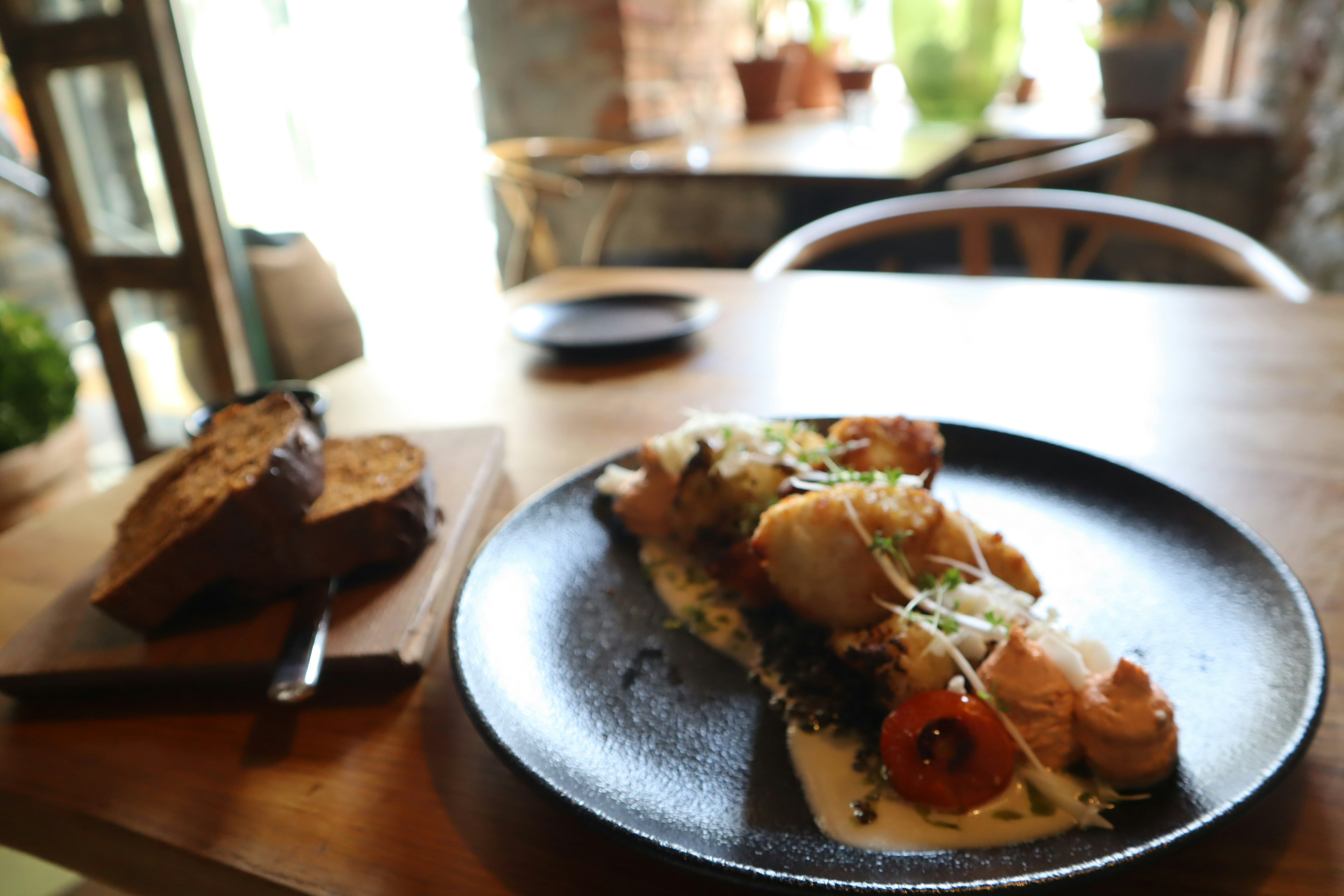 A beautifully plated dish on a black plate with a side of bread on a wooden table in a cafe